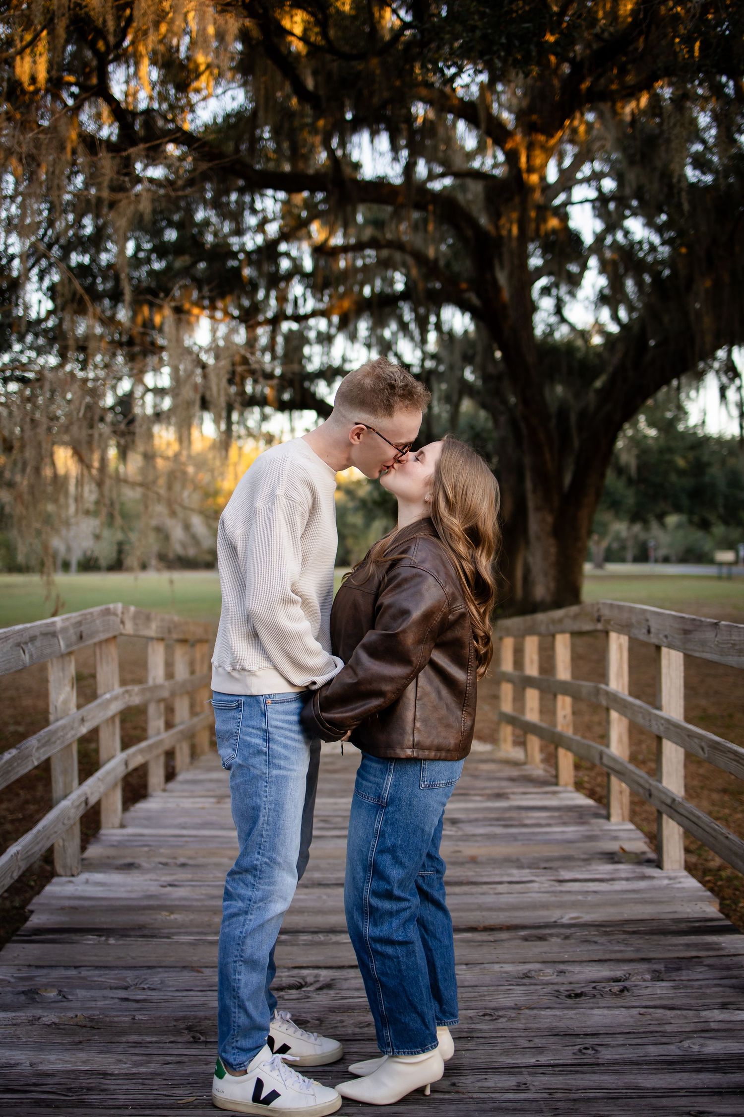 Romantic couple sharing a tender moment on a wooden bridge surrounded by Spanish moss-draped trees.