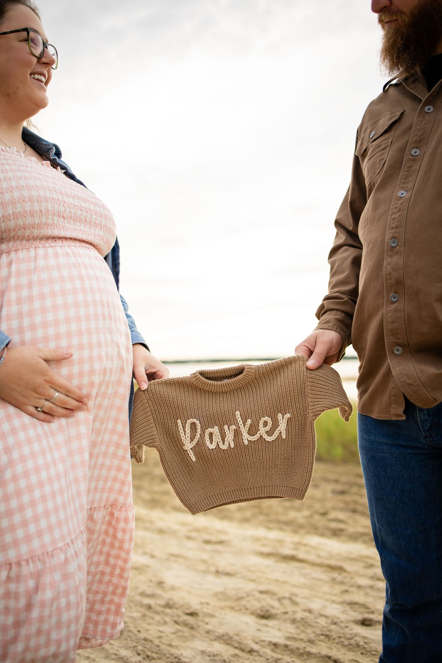 Close-up shot showing a wooden sign with 'Parker' text held against beach backdrop.
