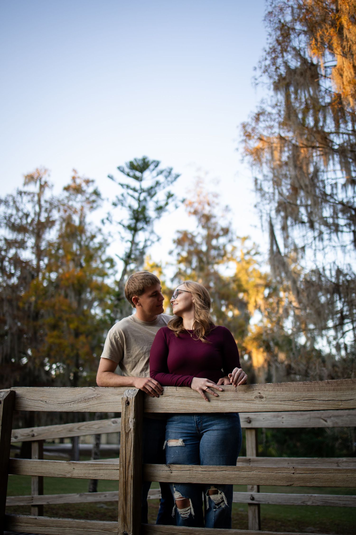 A couple shares a romantic moment on a wooden deck surrounded by autumn trees and Spanish moss at sunset.