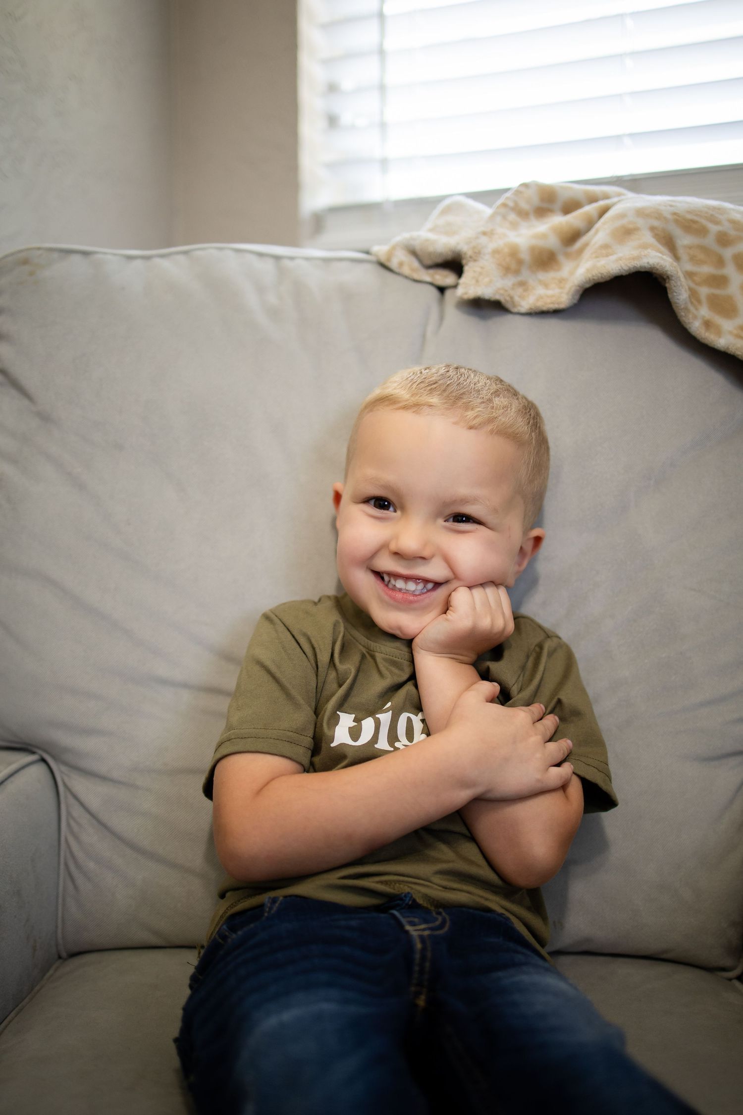 A joyful moment captured on a gray couch with a happy expression and casual olive shirt.