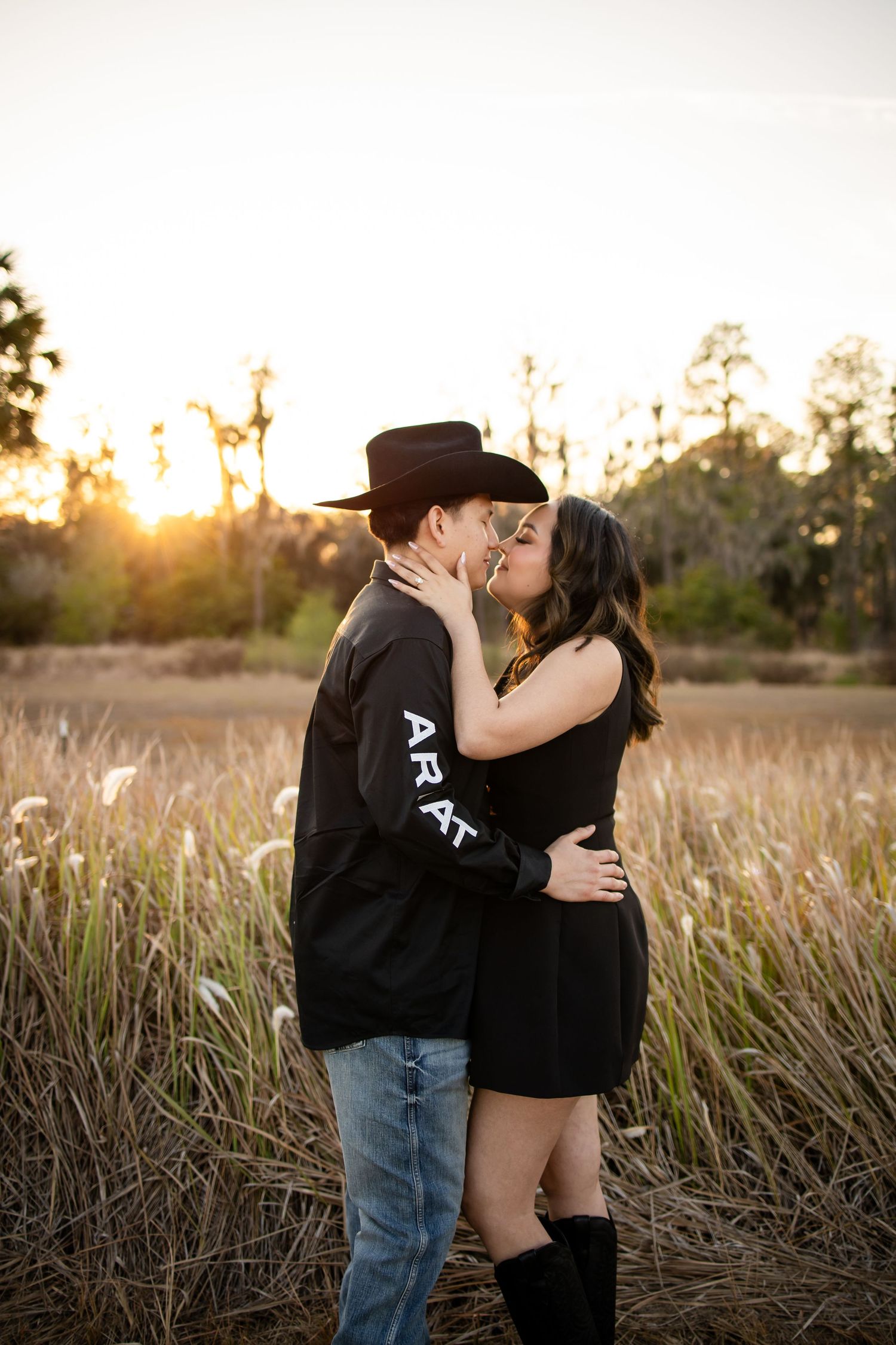 A romantic couple embraces in a field of tall grass during golden hour sunset.
