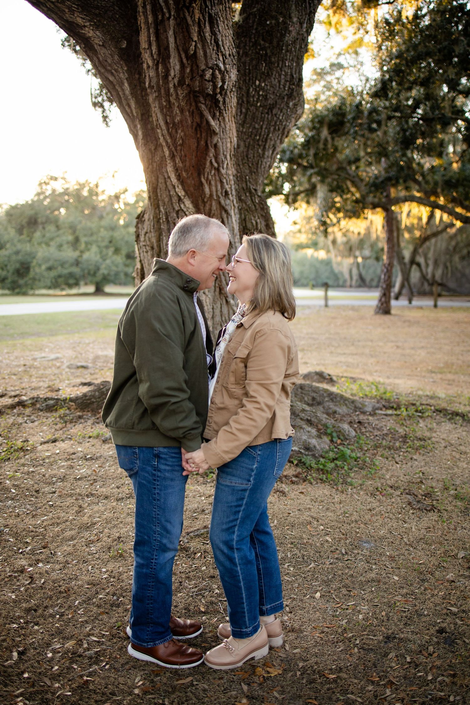 Couple in matching casual jackets share tender moment under sprawling tree.