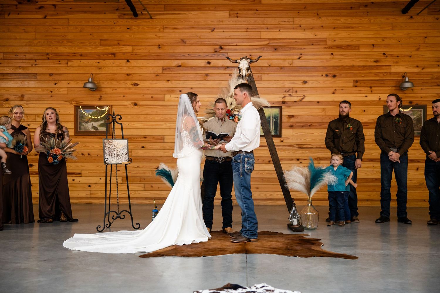Rustic barn wedding ceremony with bride and groom exchanging vows before officiant, wood walls and cowhide rug.