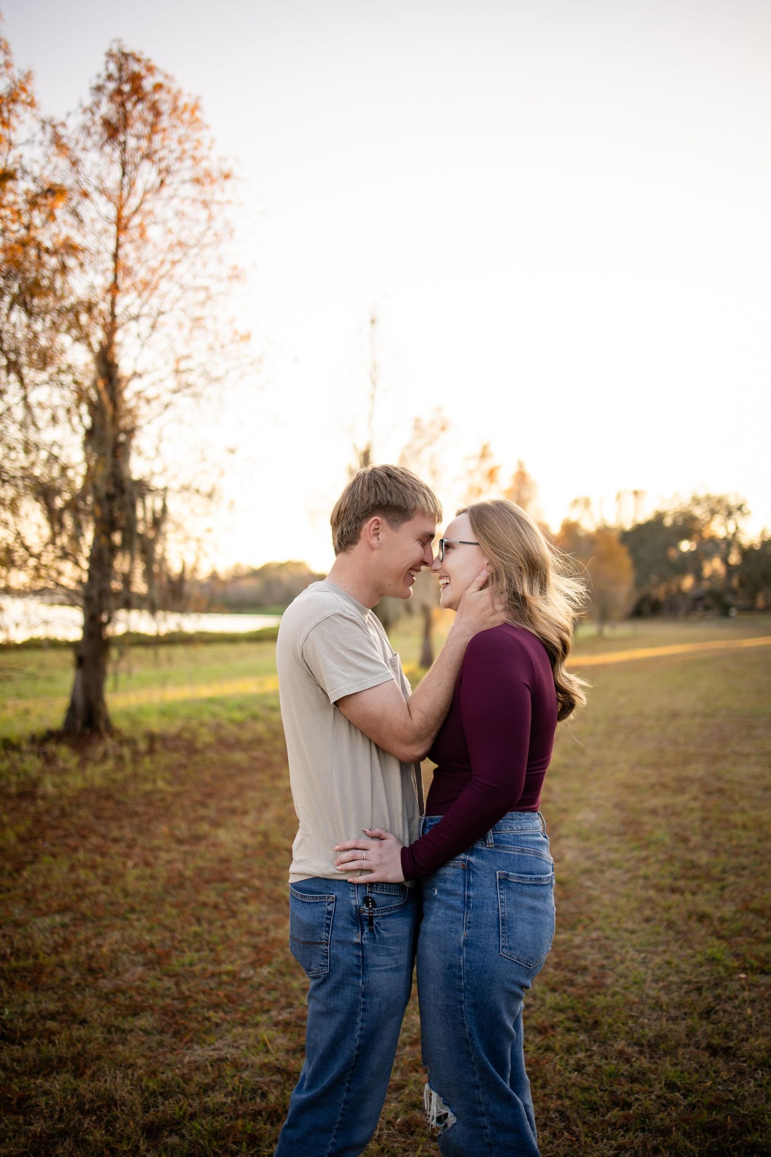 Romantic couple embraces in a golden sunset field with autumn trees in the background.