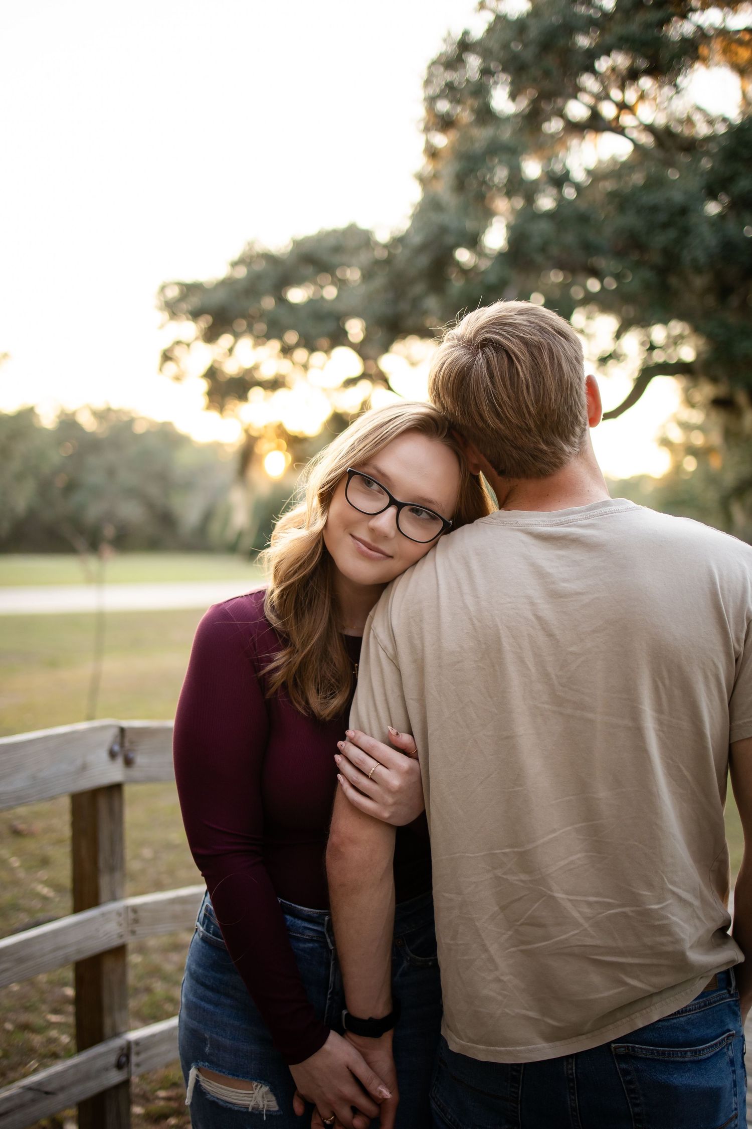 A couple shares tender moments at sunset on a wooden deck overlooking a field.