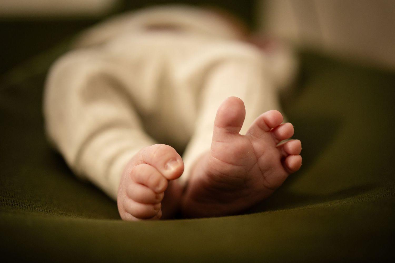Close-up of tiny baby feet resting on dark green fabric, showing soft skin and delicate toes in warm lighting.