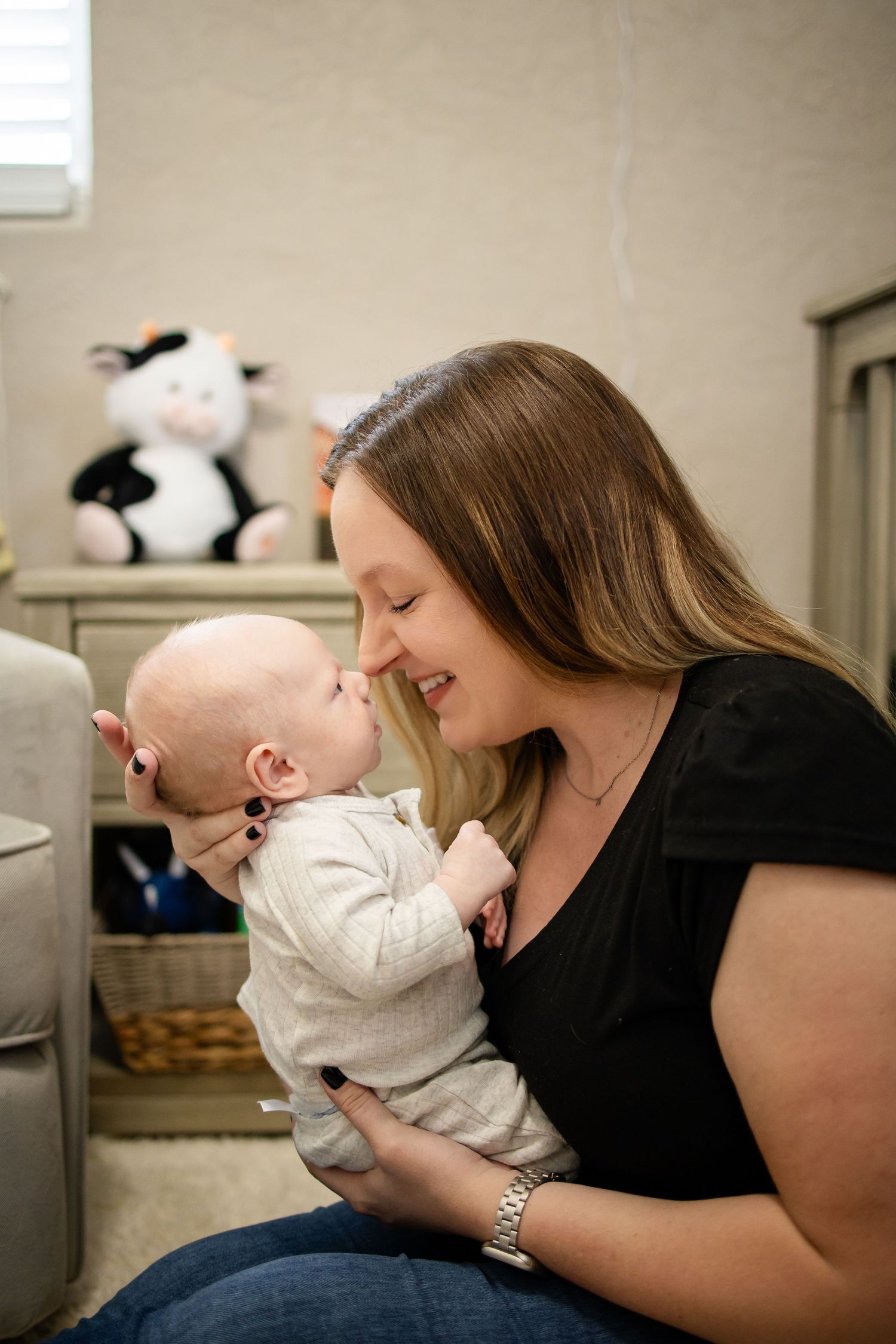 A tender loving moment as a mom in a black shirt holds and smiles with her baby in a white onesie.