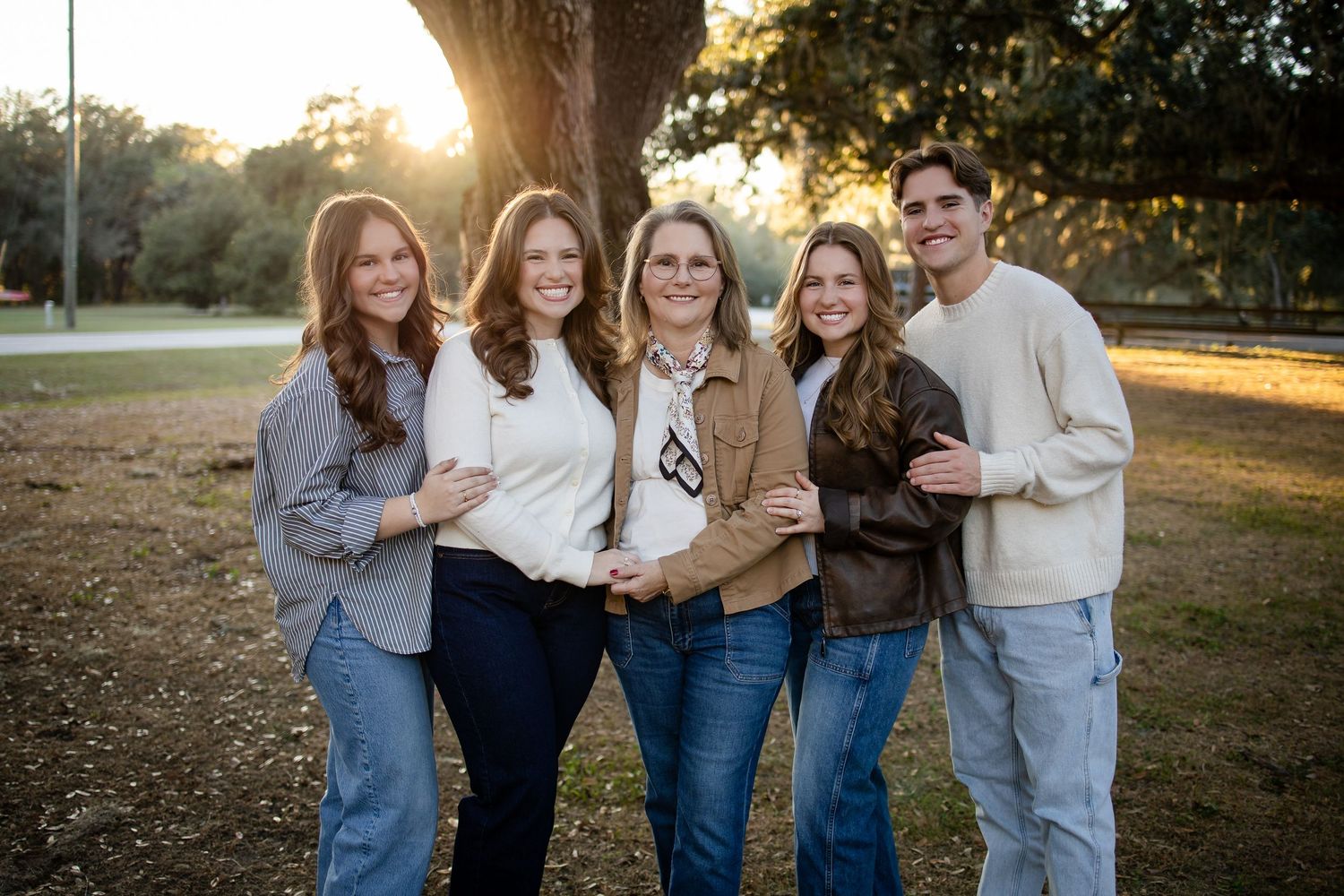Group of people in coordinated denim and neutral outfits pose together under large tree.