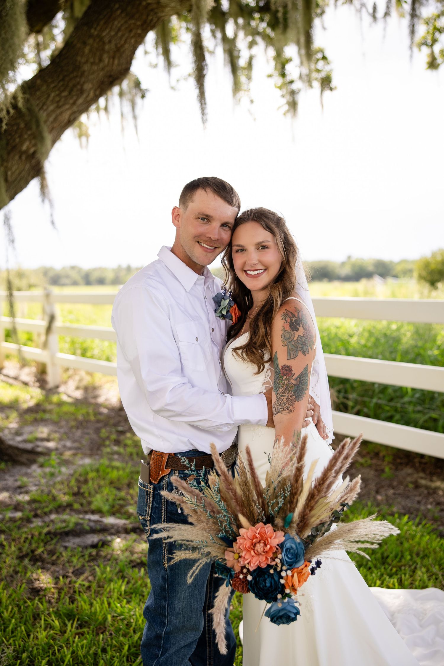 Smiling bride and groom pose under Spanish moss oak tree at outdoor farm wedding venue.