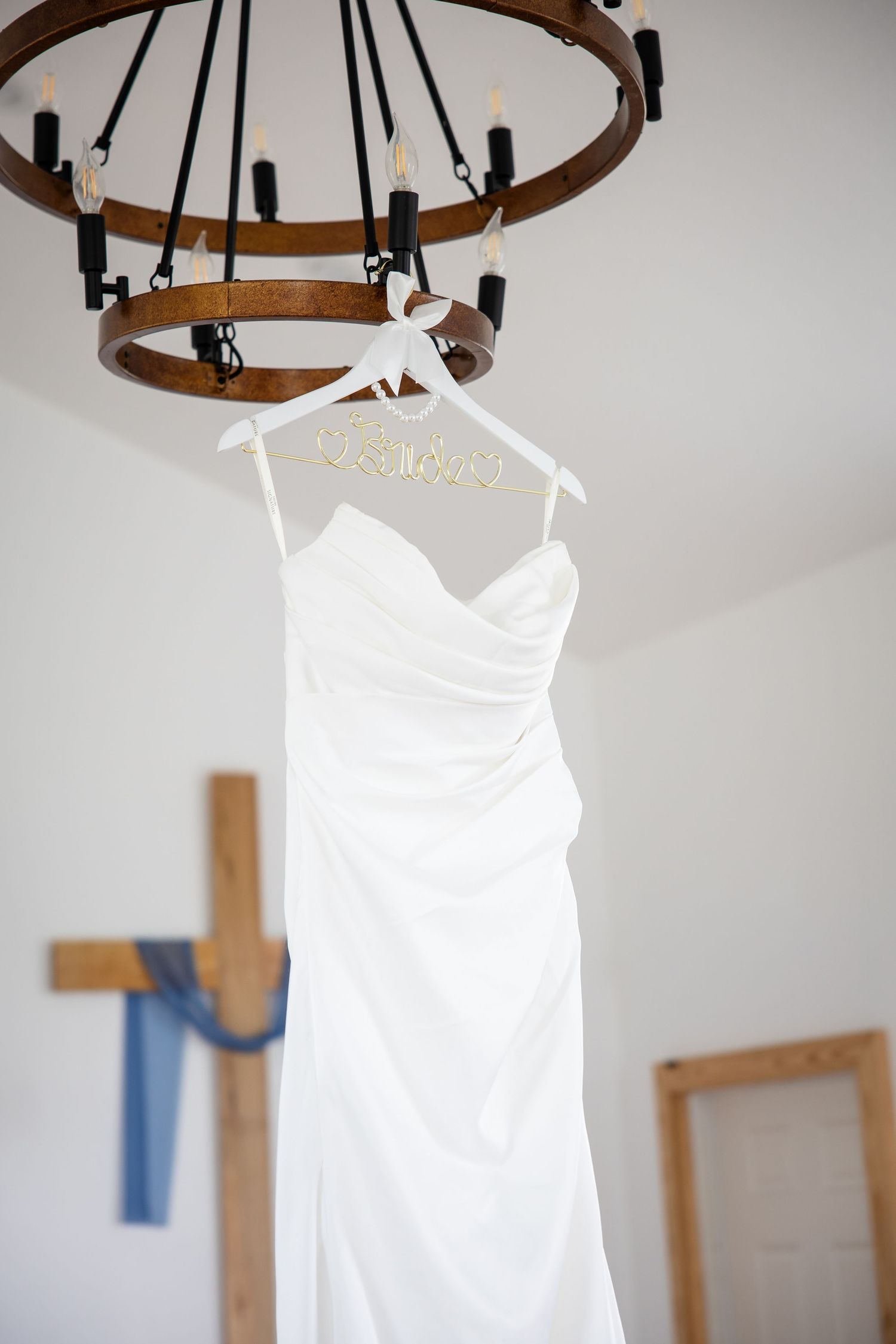 White wedding dress on personalized hanger displayed on rustic chandelier in bright bridal suite.