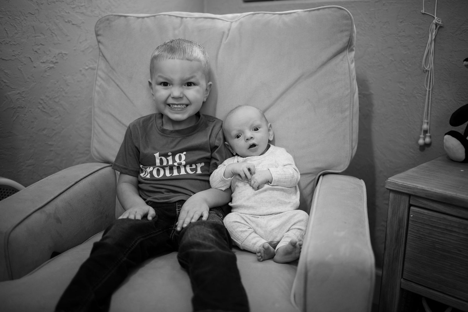 Black and white portrait of two young children sitting together on a large couch cushion.