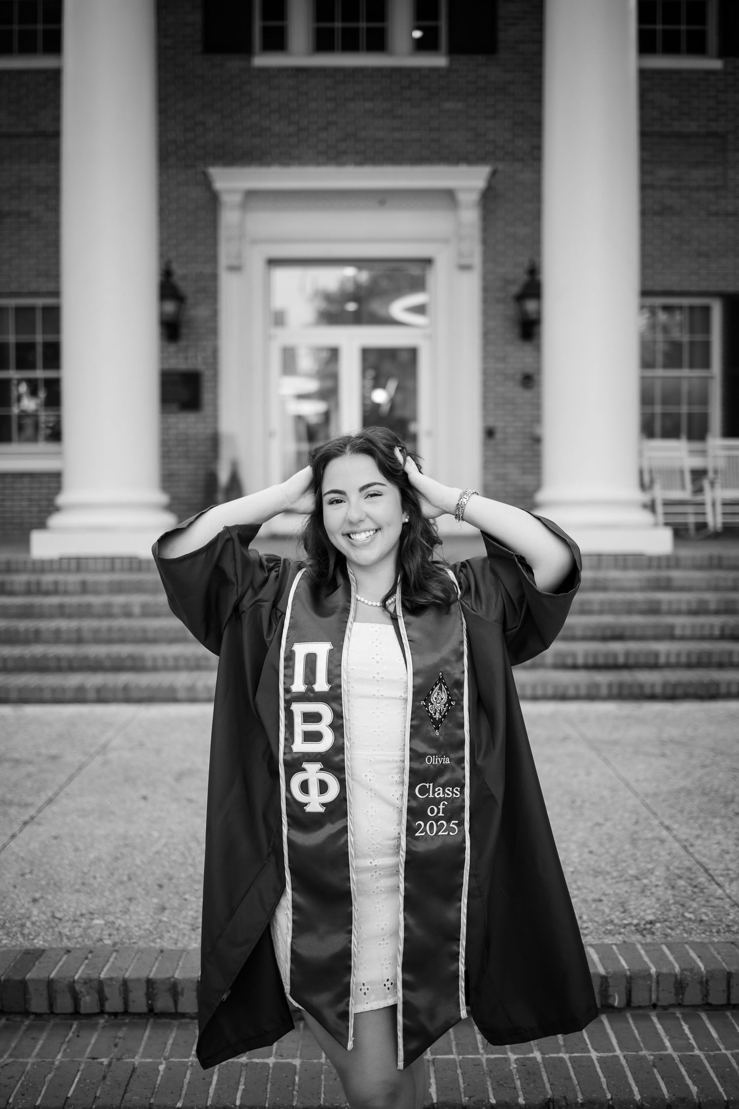 Black and white graduation portrait showing a joyful pose wearing academic regalia and Greek organization stole.