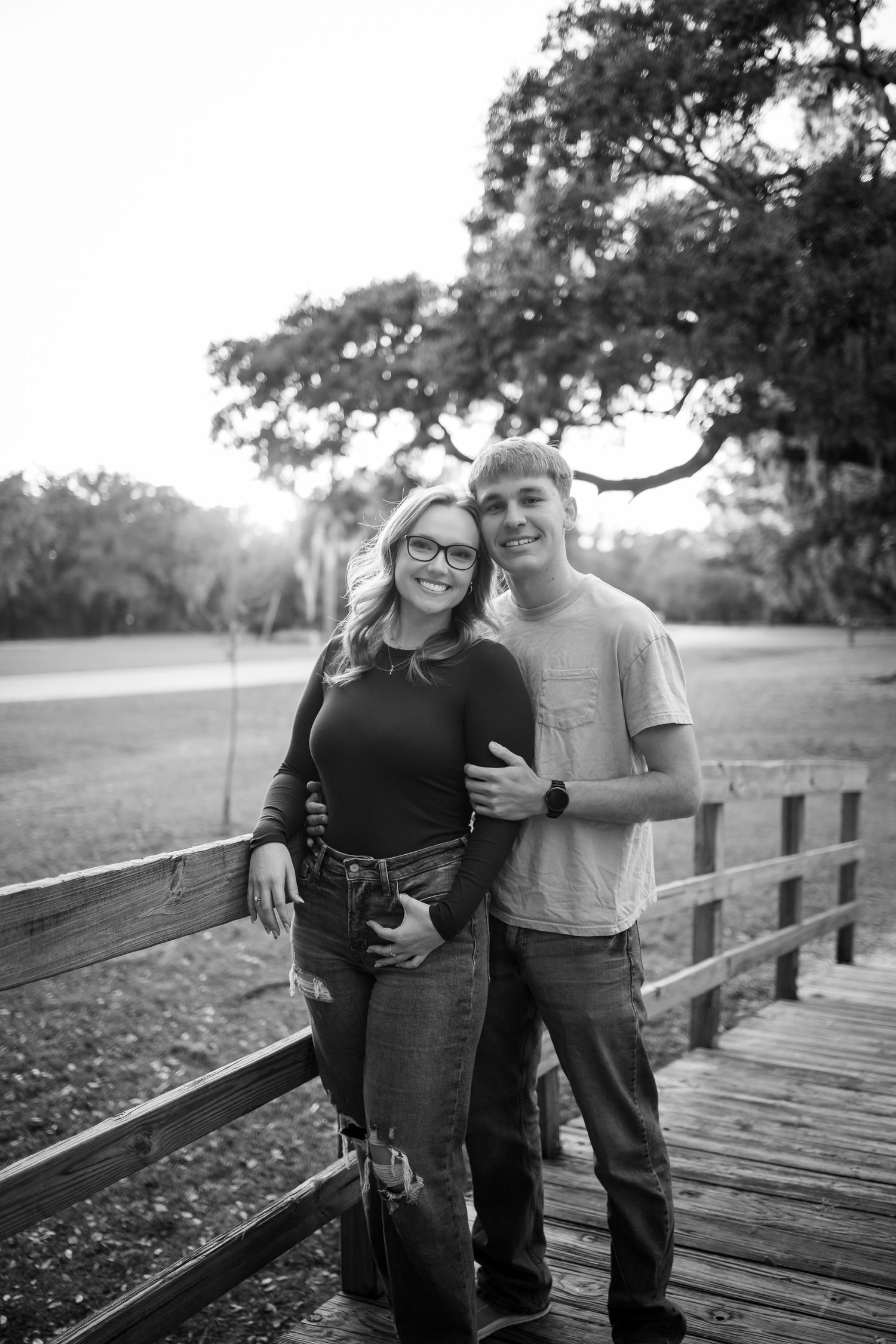 A couple poses together on a wooden boardwalk with Spanish moss draped trees in the background.