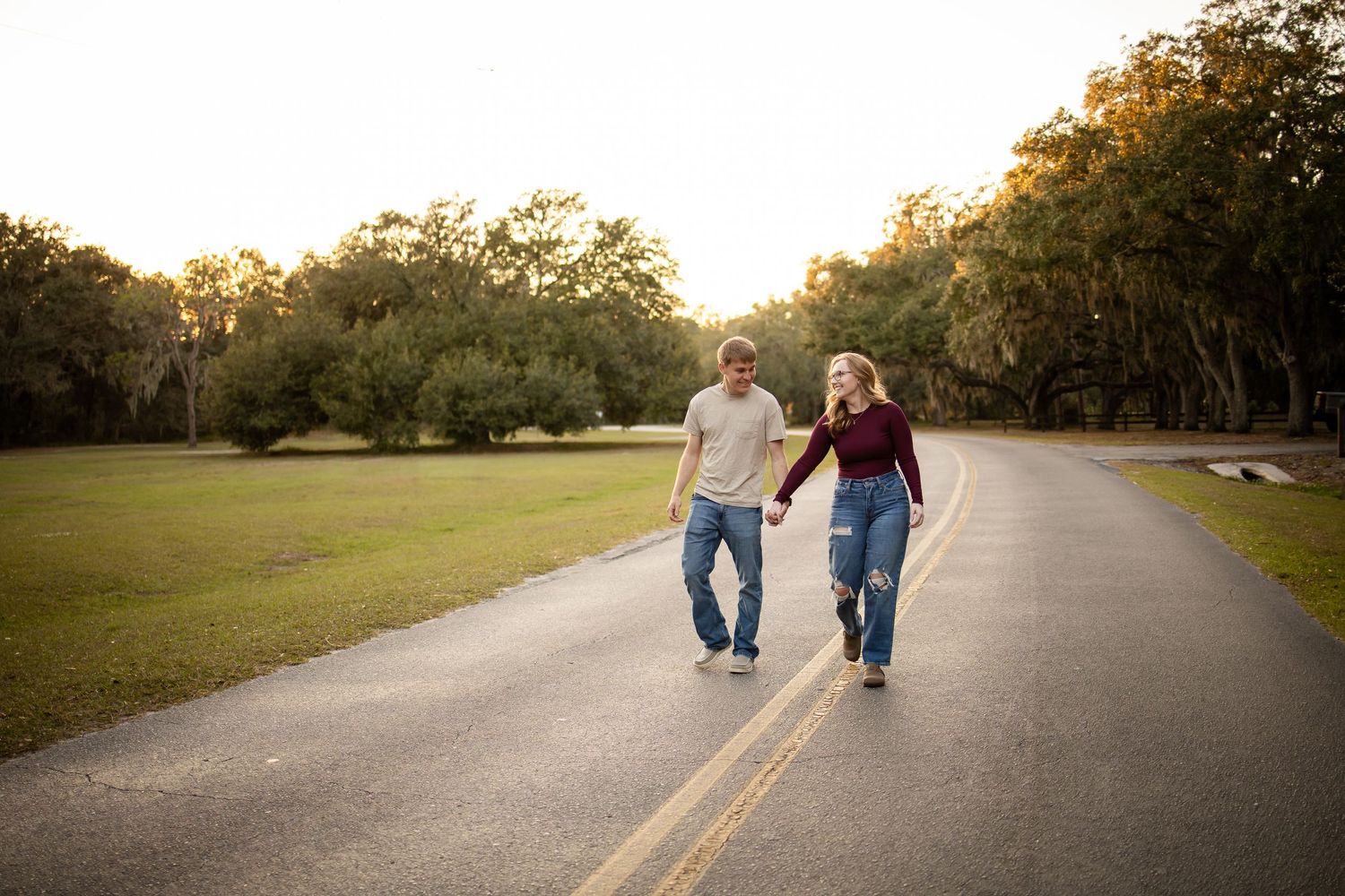 Couple walking hand in hand down a tree-lined road at sunset.