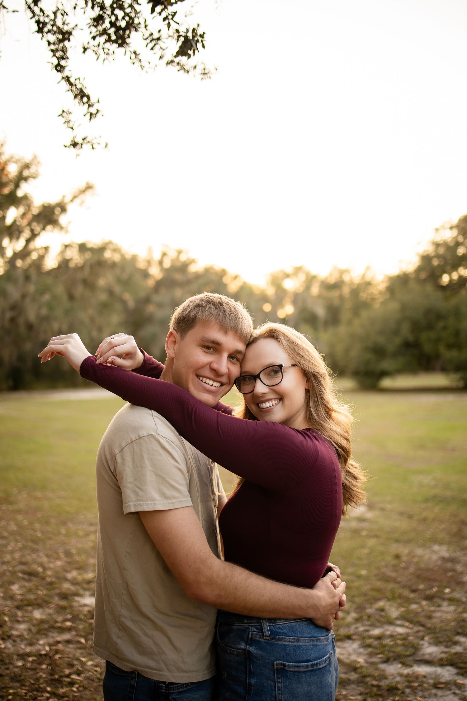 A joyful couple embraces and laughs together in a sunlit field during golden hour.