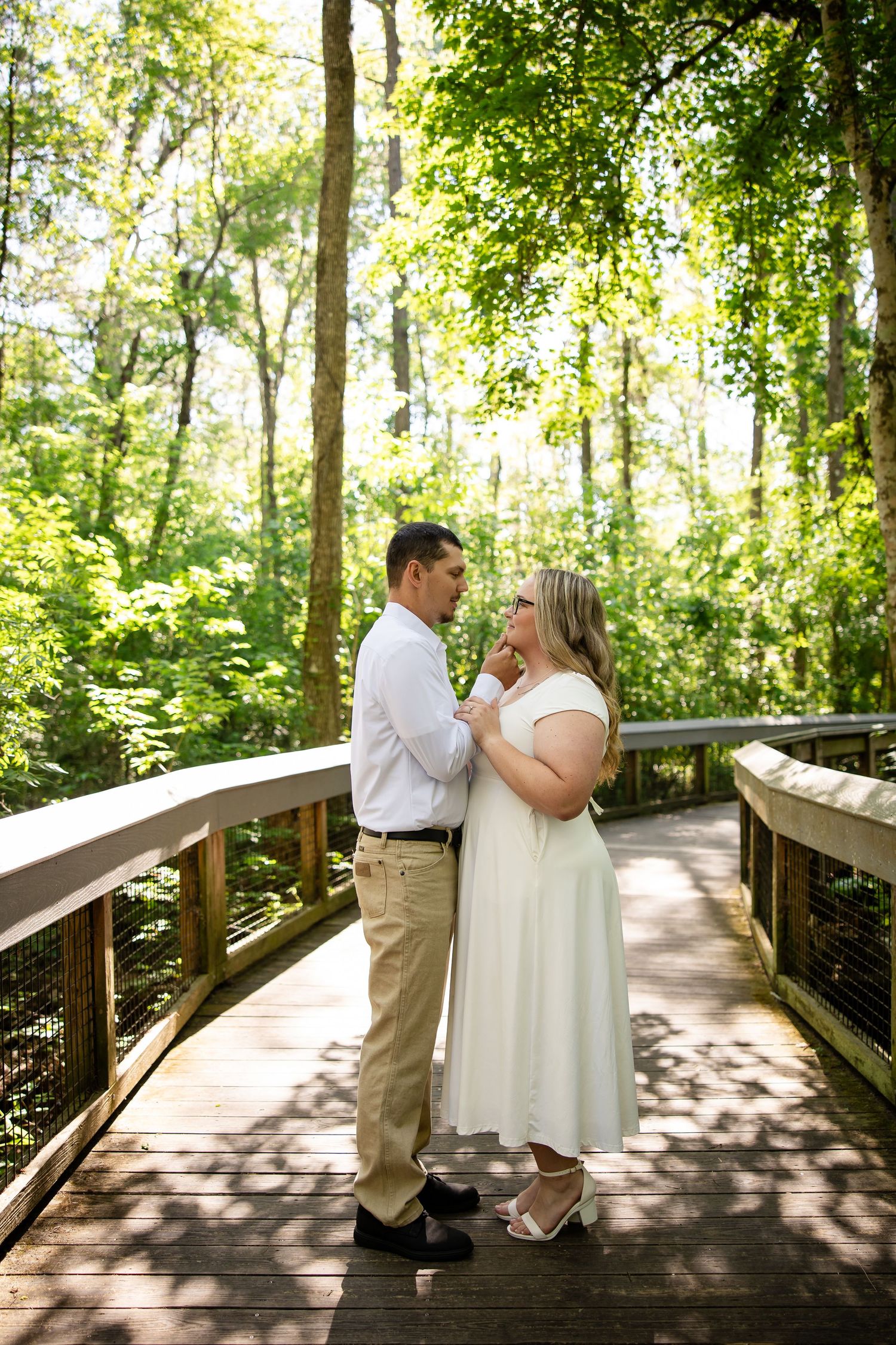 Couple sharing a romantic moment on a wooden boardwalk surrounded by lush green forest trees.
