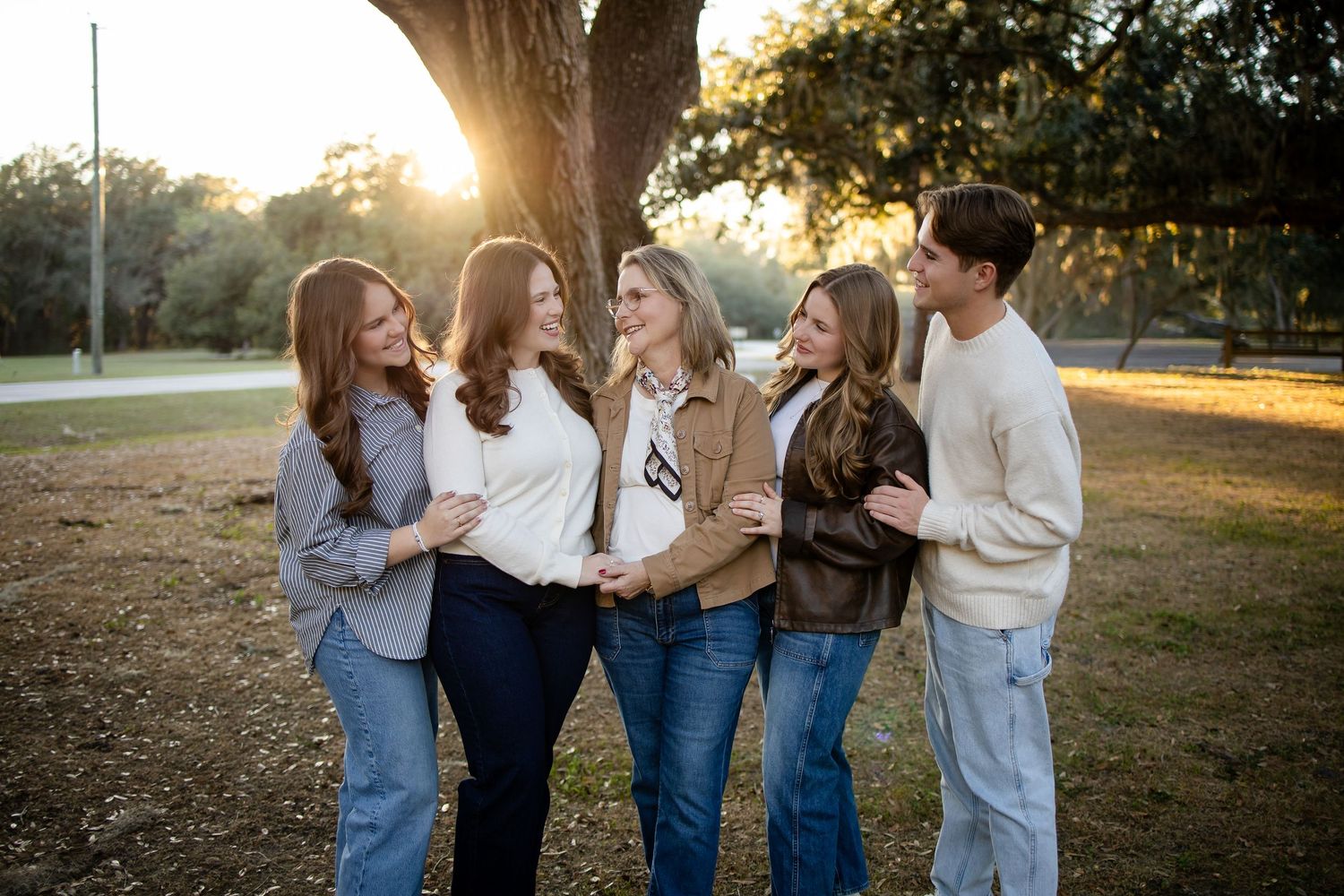 A group of friends laugh together while standing under a large tree at golden hour.