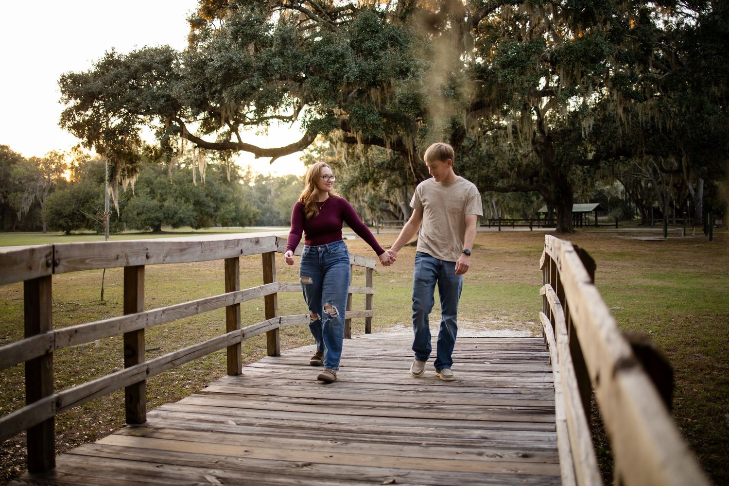 Two people walking away on a wooden boardwalk surrounded by trees in late afternoon light.