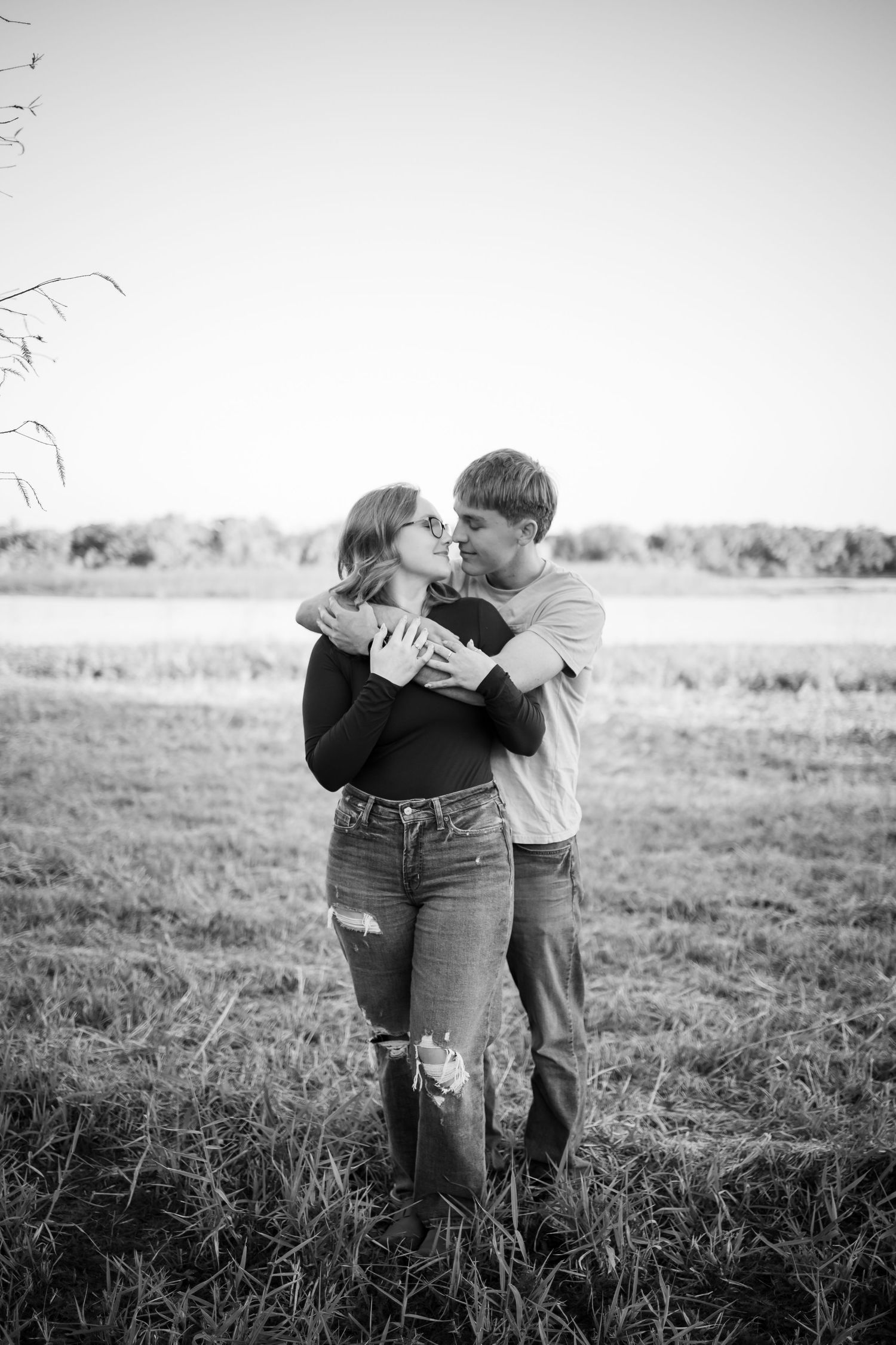 A romantic black and white photo of a couple embracing in a sunlit field.