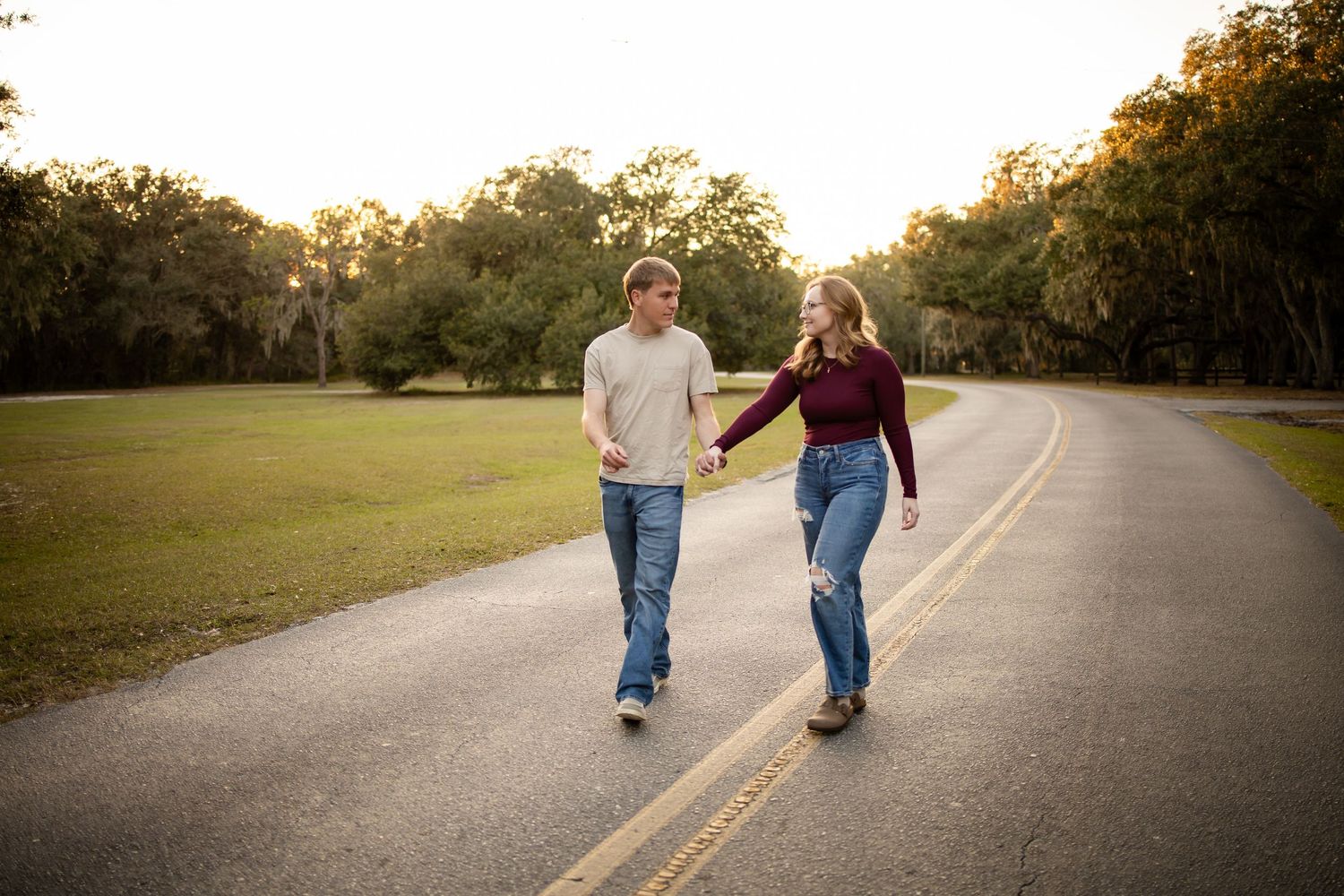 Couple walking together on a tree-lined road during golden hour.