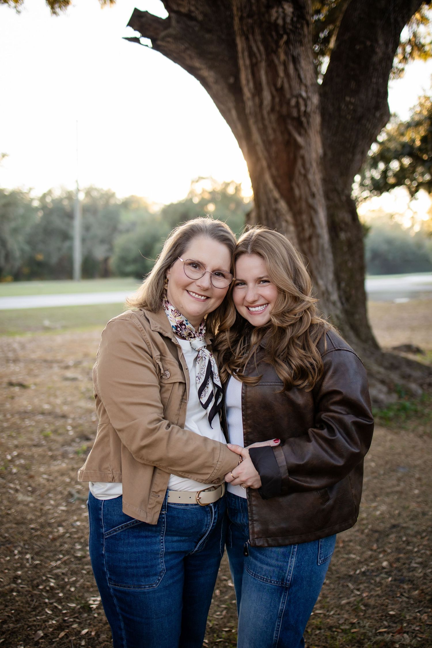 Two people in matching denim and jackets share laughter under large oak trees.