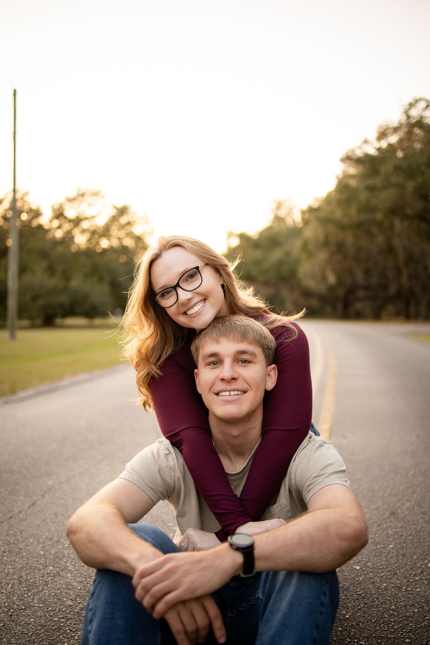 Couple posing playfully on asphalt road during golden hour.