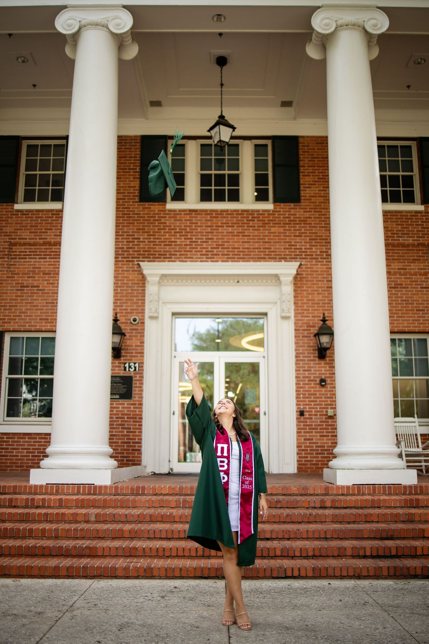 A person in graduation attire stands on brick steps with white ionic columns of a stately building entrance in multiple poses.