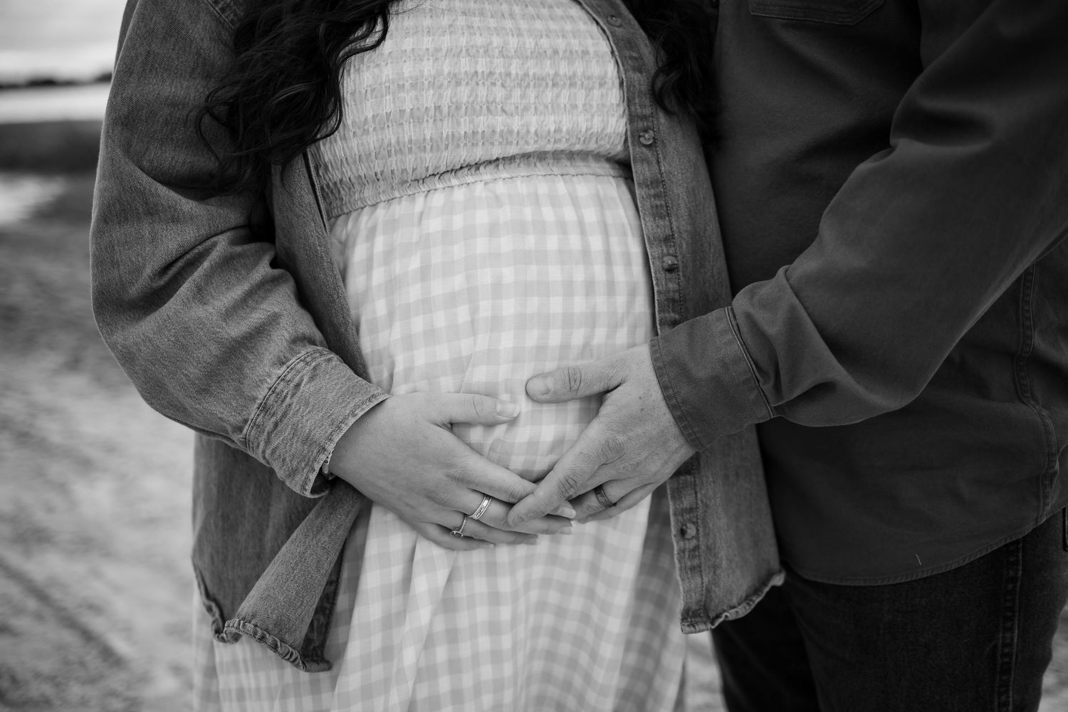 Black and white maternity photo showing hands cradling a pregnant belly in a gingham dress.