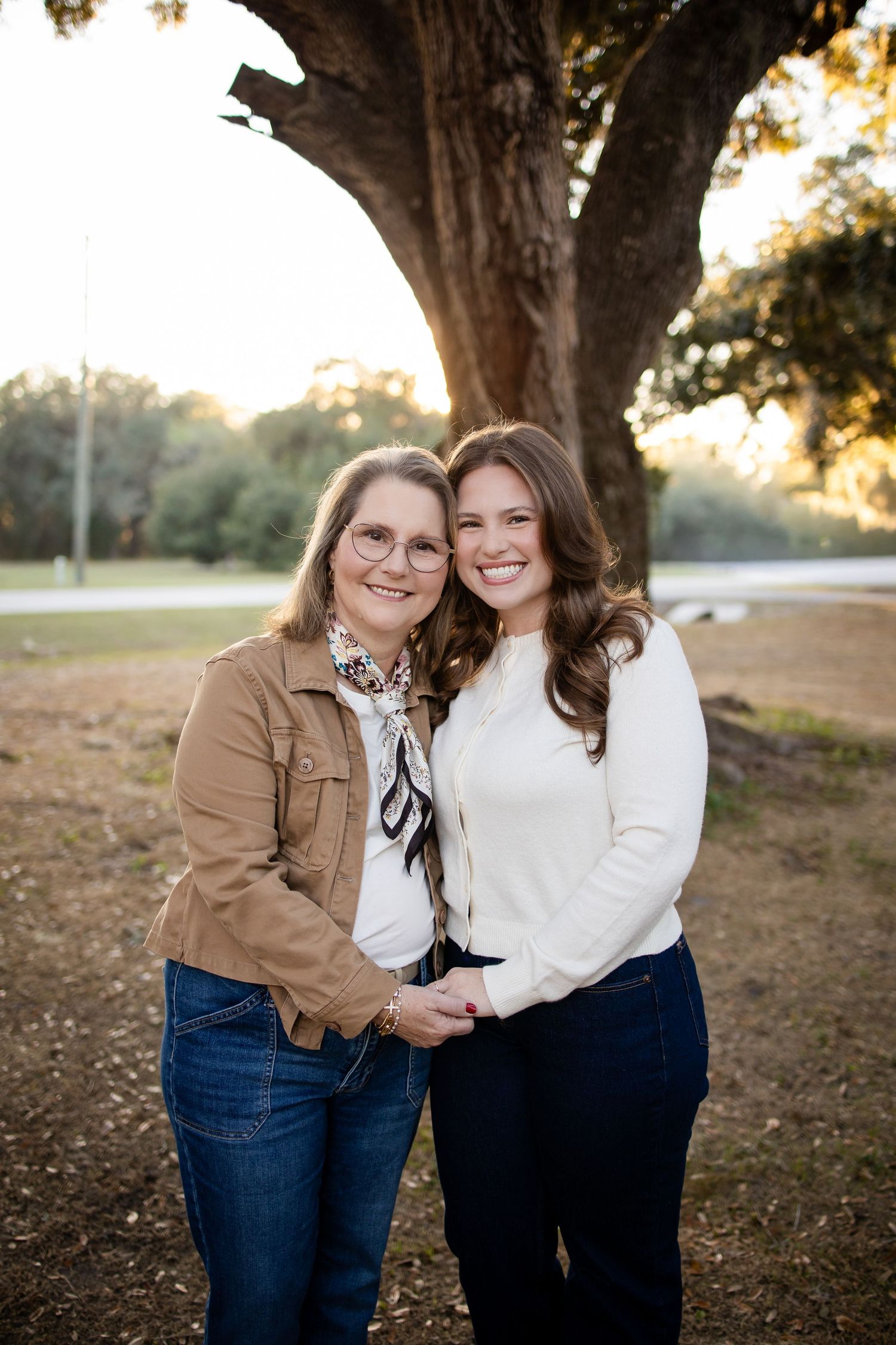 Two people in casual attire pose together under a large oak tree at sunset.