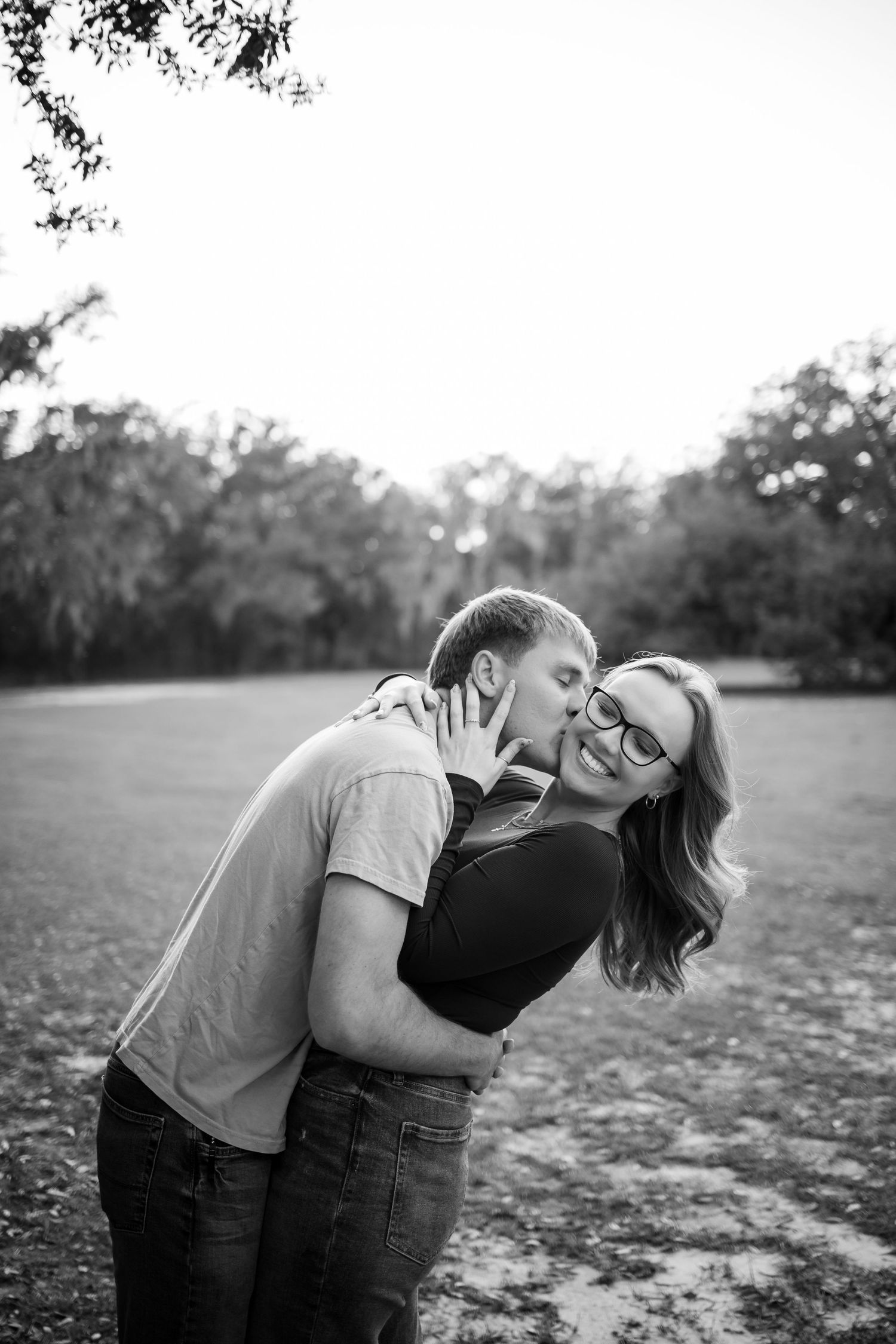 A black and white photo of a couple sharing a playful moment outdoors.