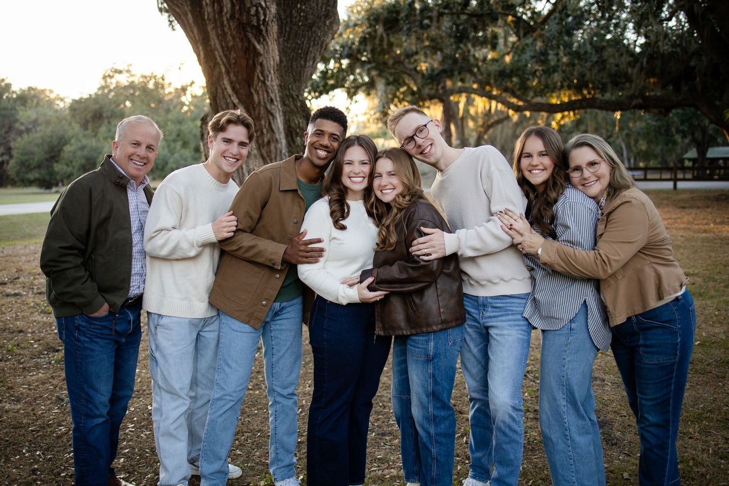 Group photo of friends in coordinated denim and neutral colors standing together under trees at dusk.