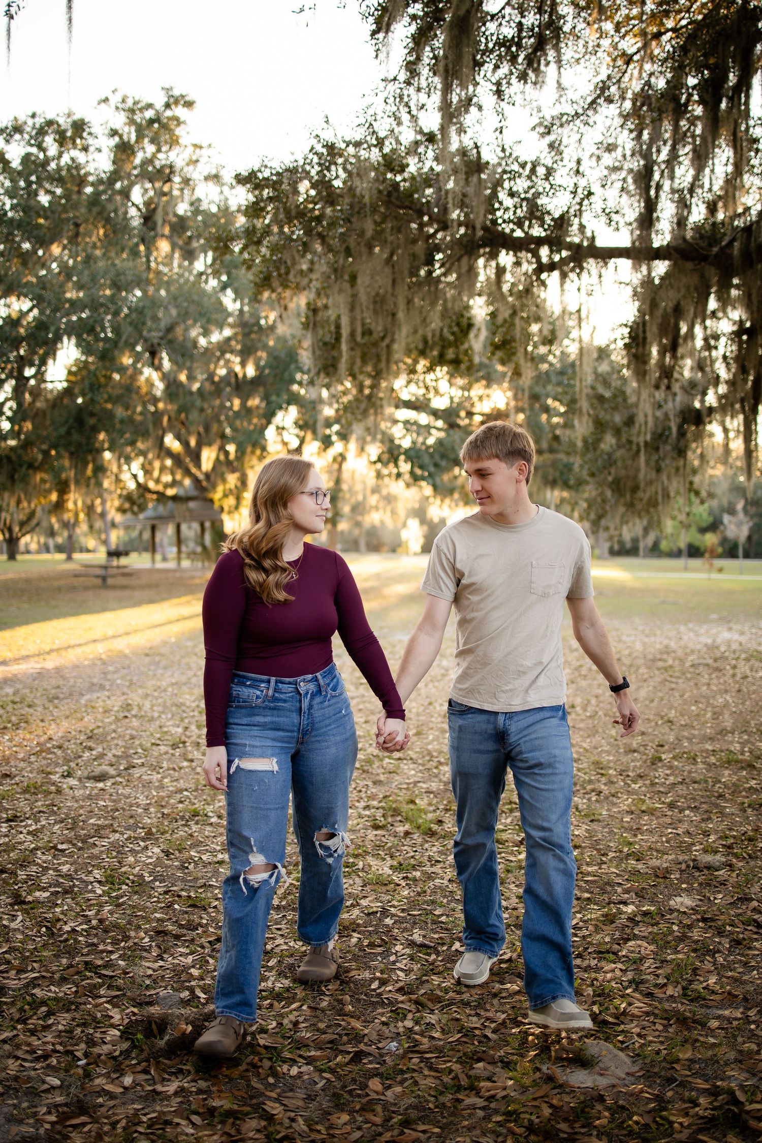 A couple walking hand in hand through fallen autumn leaves in a park at sunset.