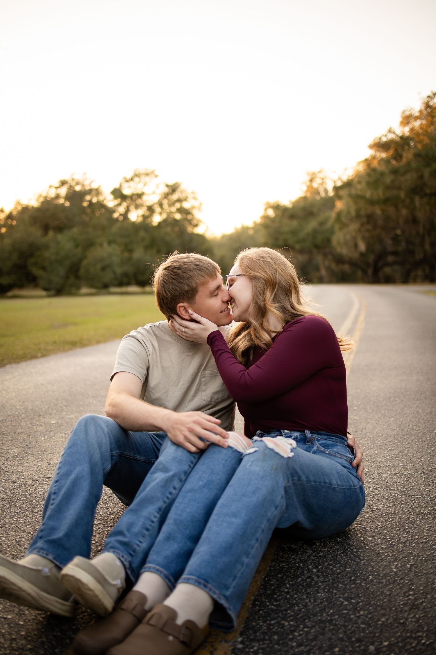 Couple sharing tender moments while sitting on asphalt road at sunset.