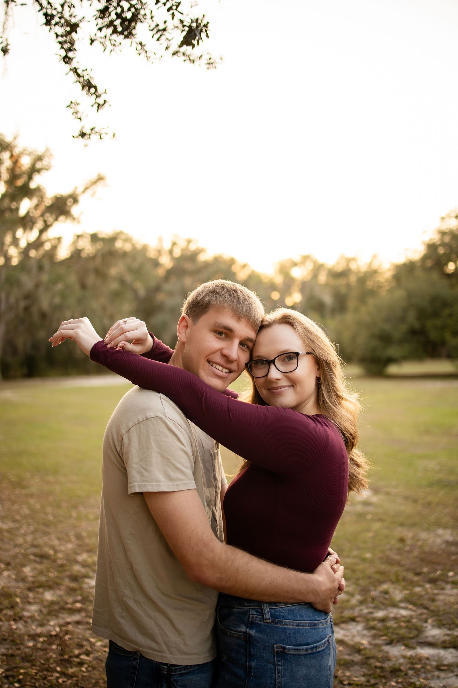 Happy couple in casual wear hugging and smiling during sunset in a park setting.