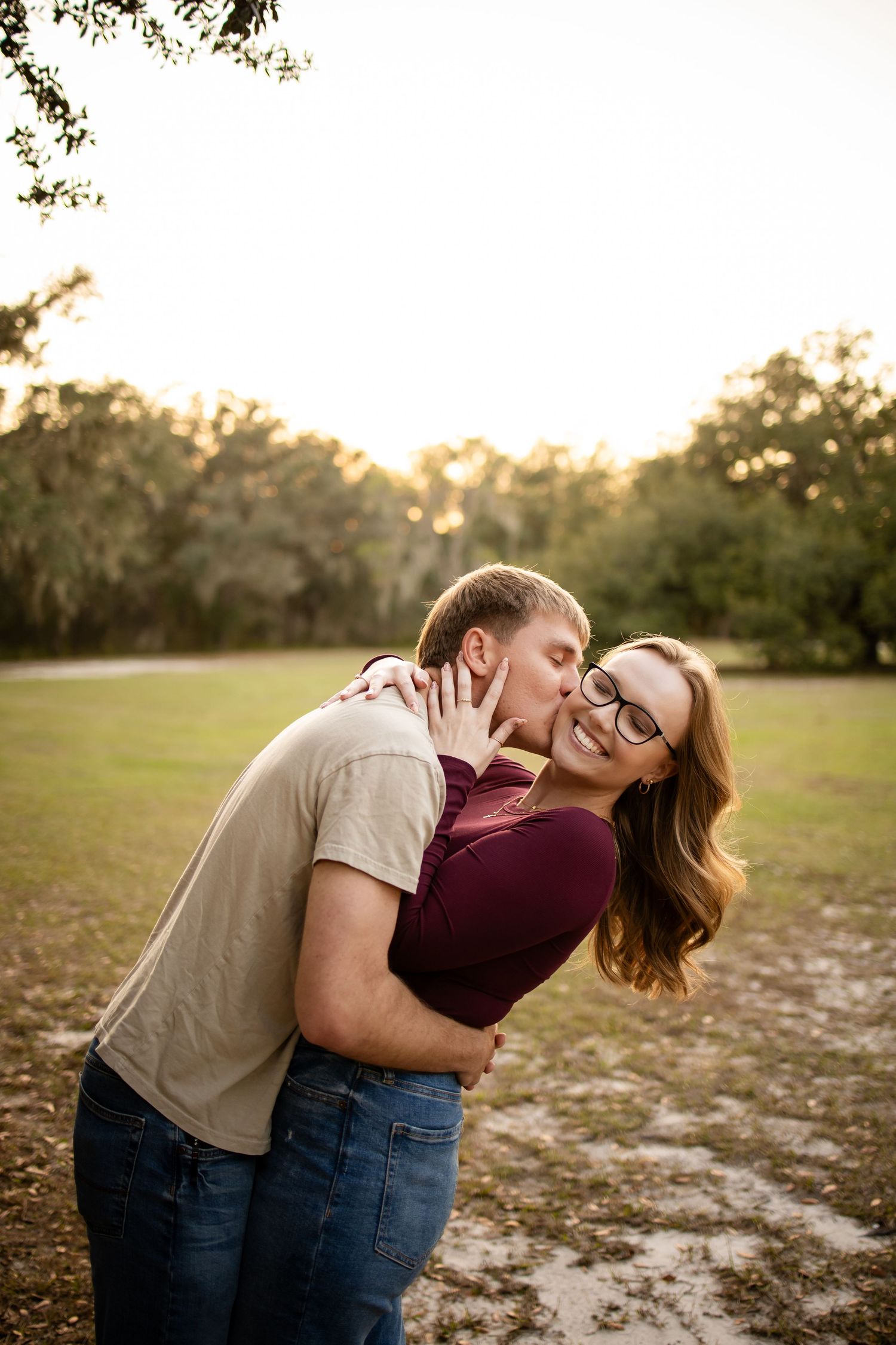 A couple shares a tender moment in a field during golden hour while wearing casual attire.