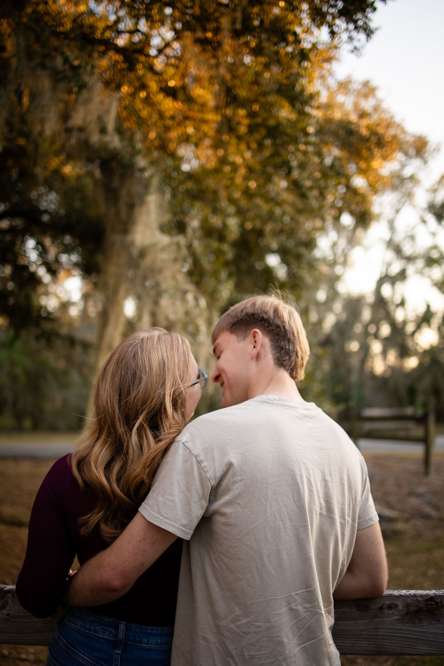Couple sharing tender moment on wooden bench surrounded by autumn trees at golden hour.