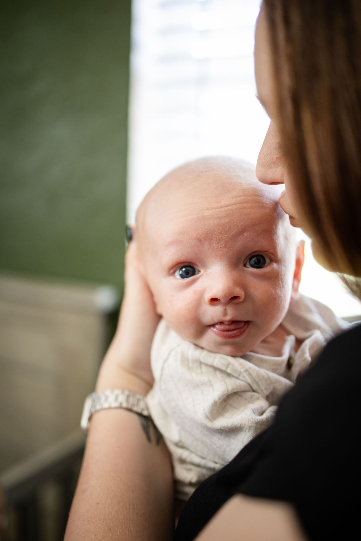 A tender moment shows a baby in a white onesie gazing while being held by someone wearing black.
