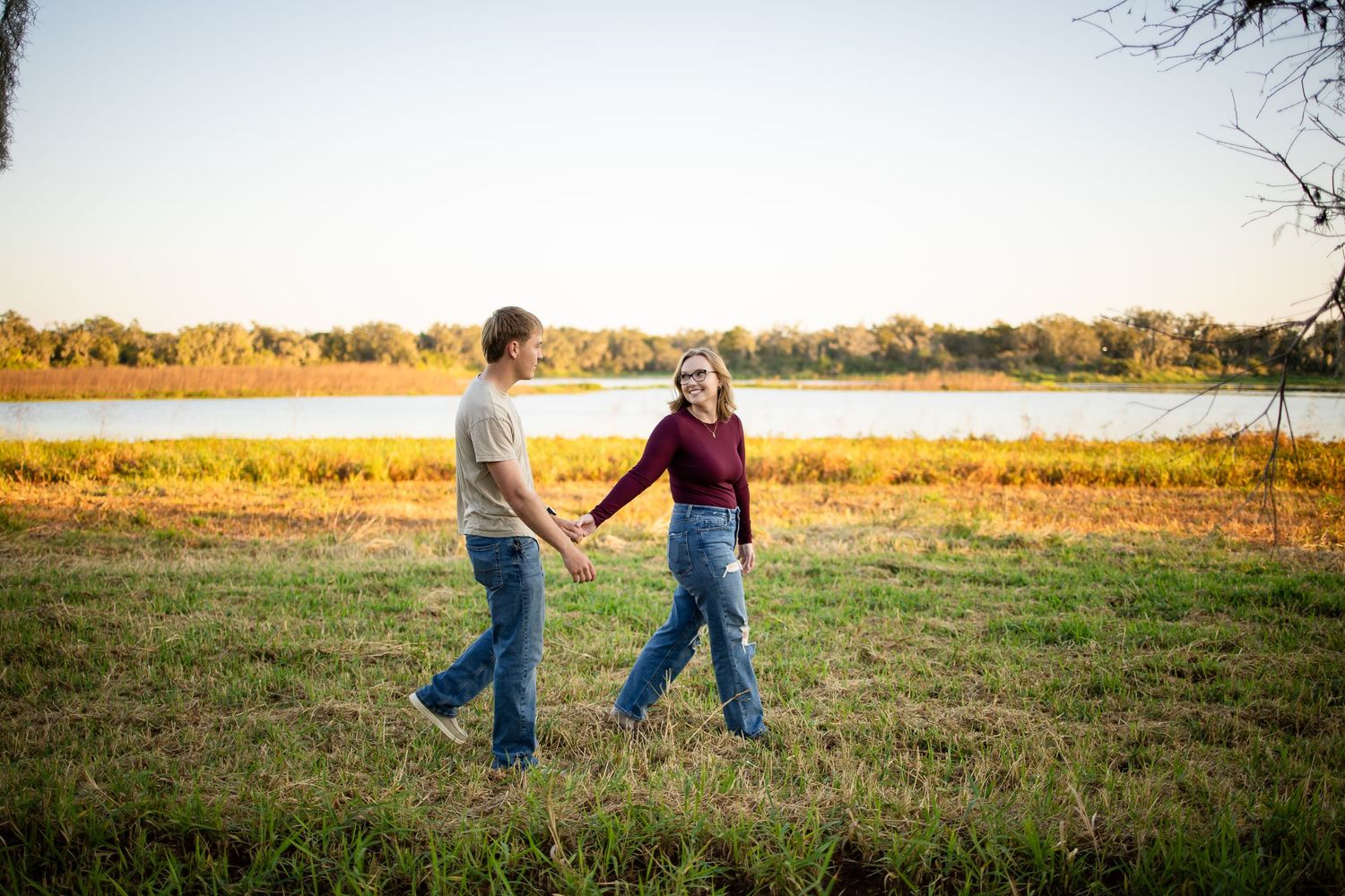 Two people walking together across a golden field at sunset with trees in the background.