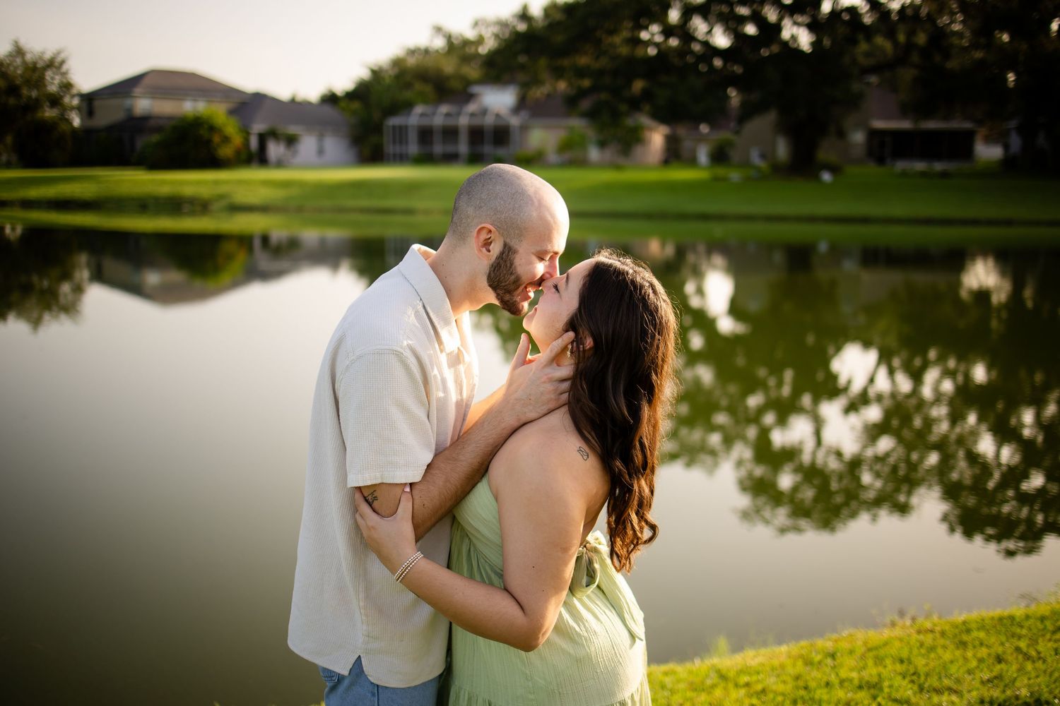 A romantic moment between two people embracing near a tranquil pond at sunset.