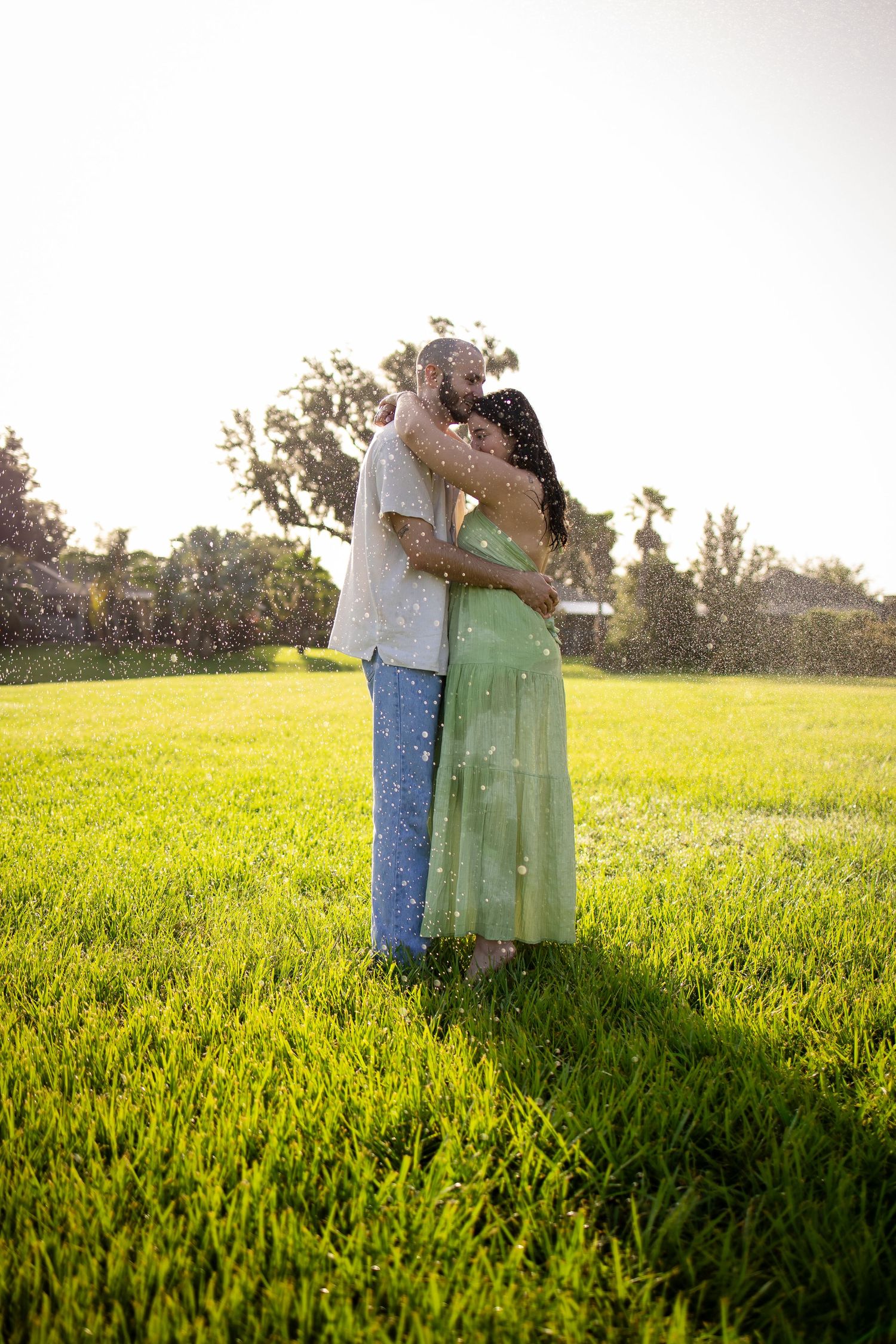 A couple shares an intimate moment together in a sun-drenched green meadow at golden hour.