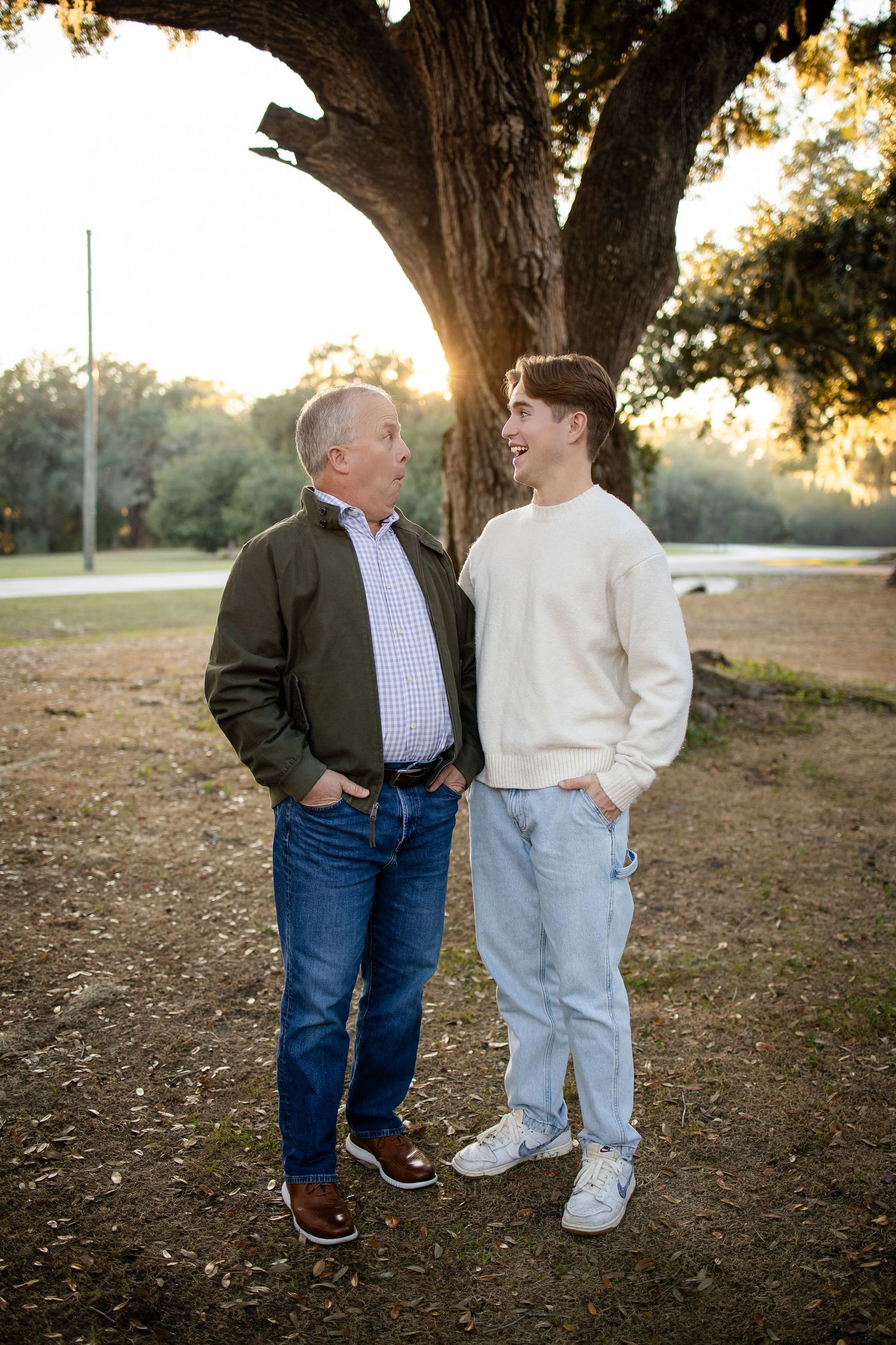 Two people in casual attire share a moment while standing under large tree at sunset.