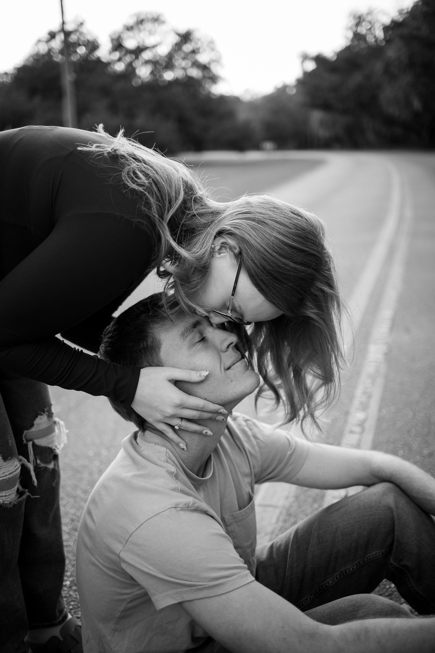 An intimate black and white portrait of a couple sharing a tender moment on a country road.