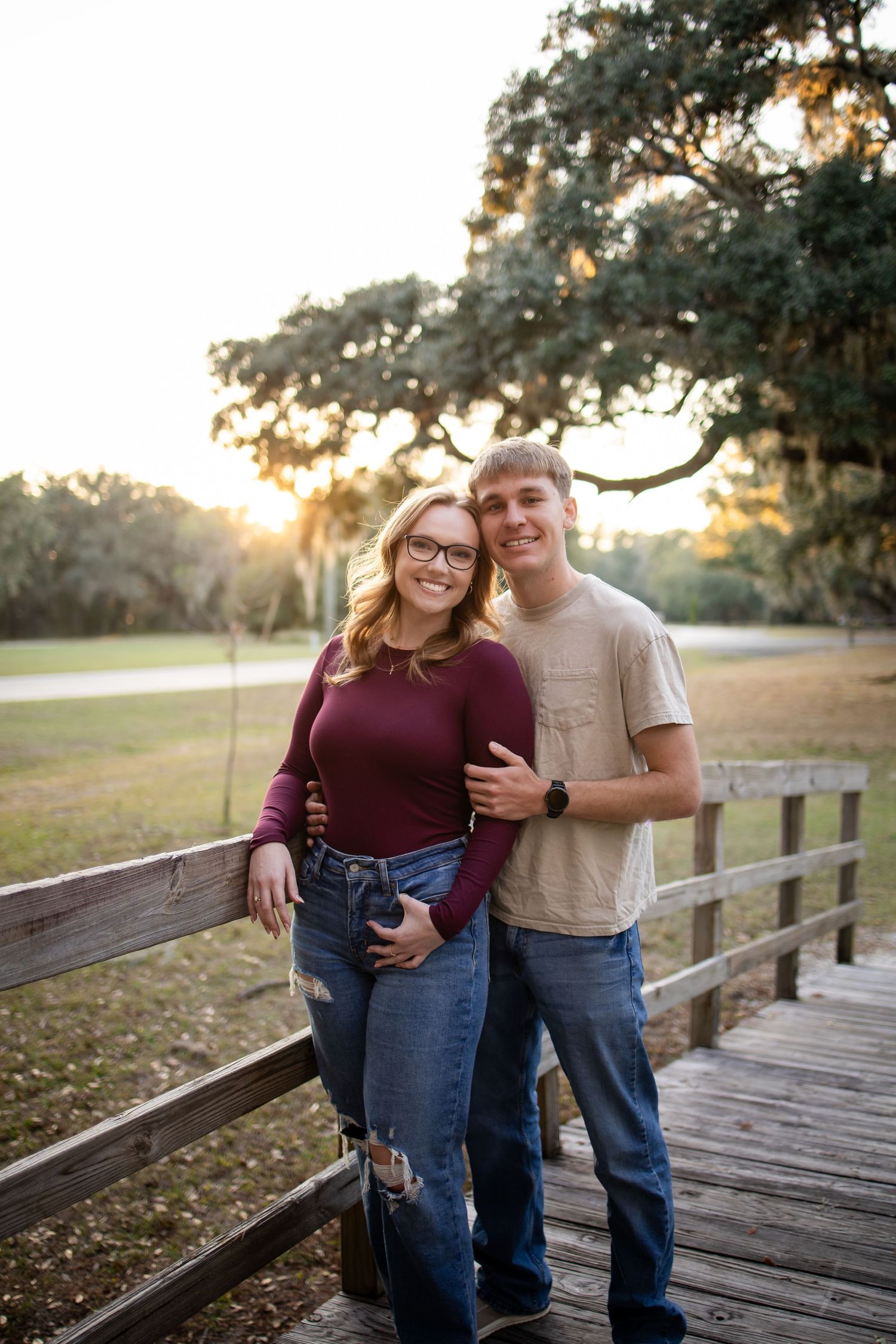 A couple poses together on a wooden boardwalk during golden hour with Spanish moss trees behind them.