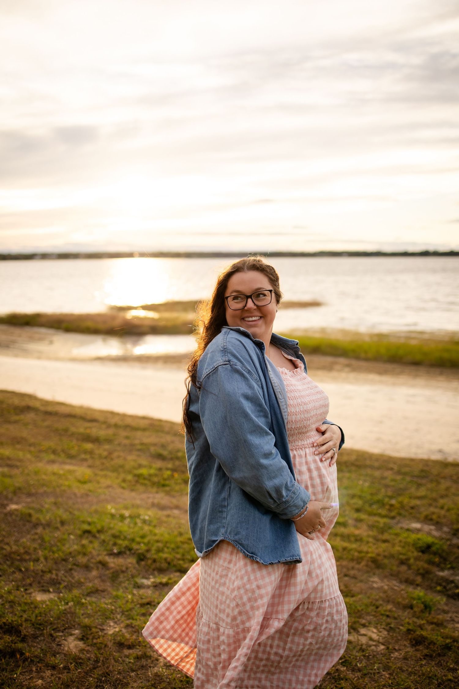 Joyful maternity photo session on beach with water and sunset in background.