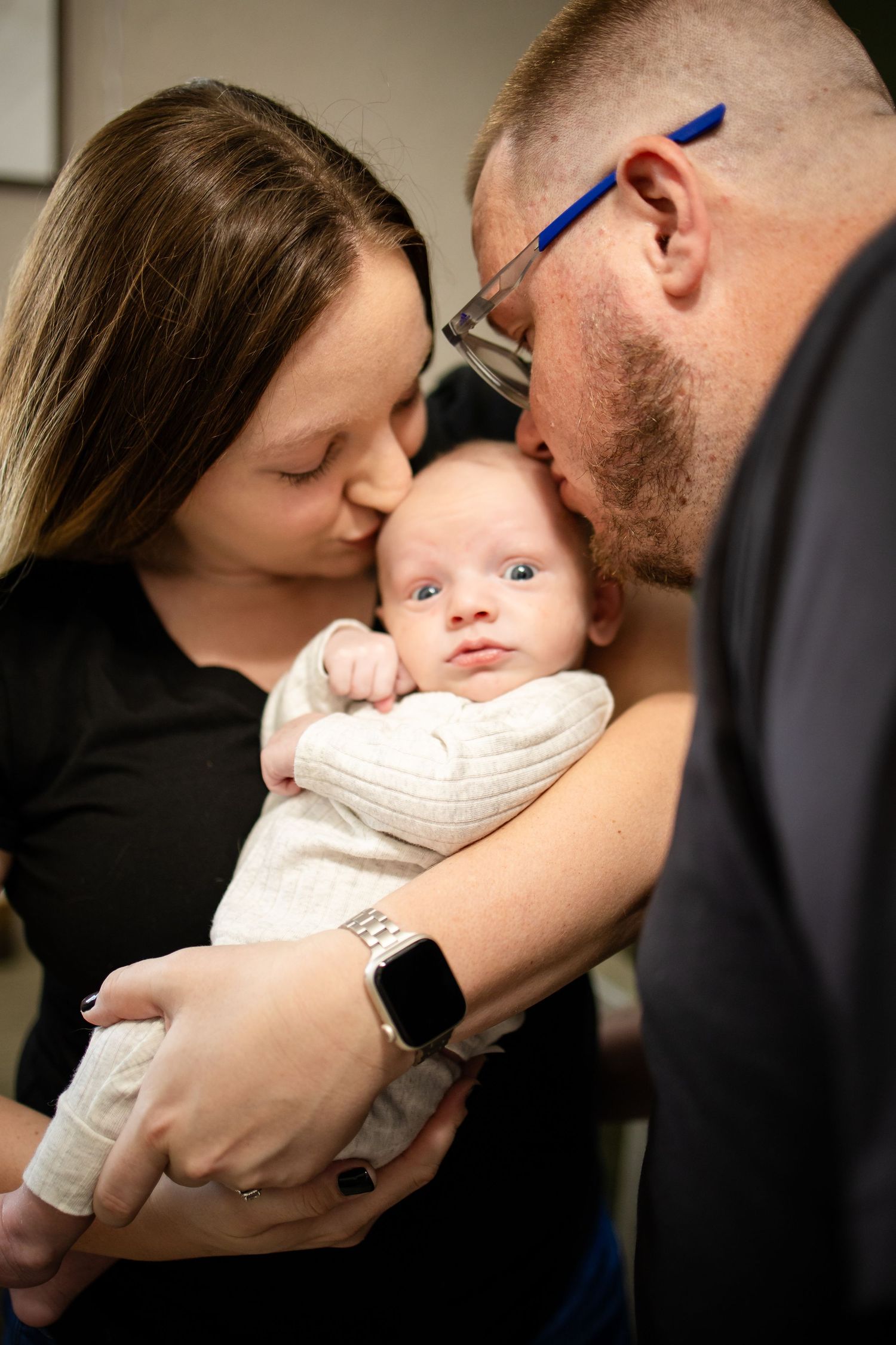 A tender family moment as parents cuddle their newborn infant dressed in white.