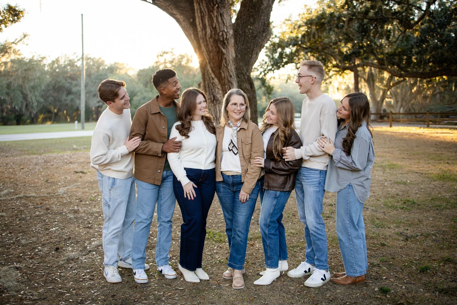 Friends in casual outfits gather for a group photo under a moss-draped tree.