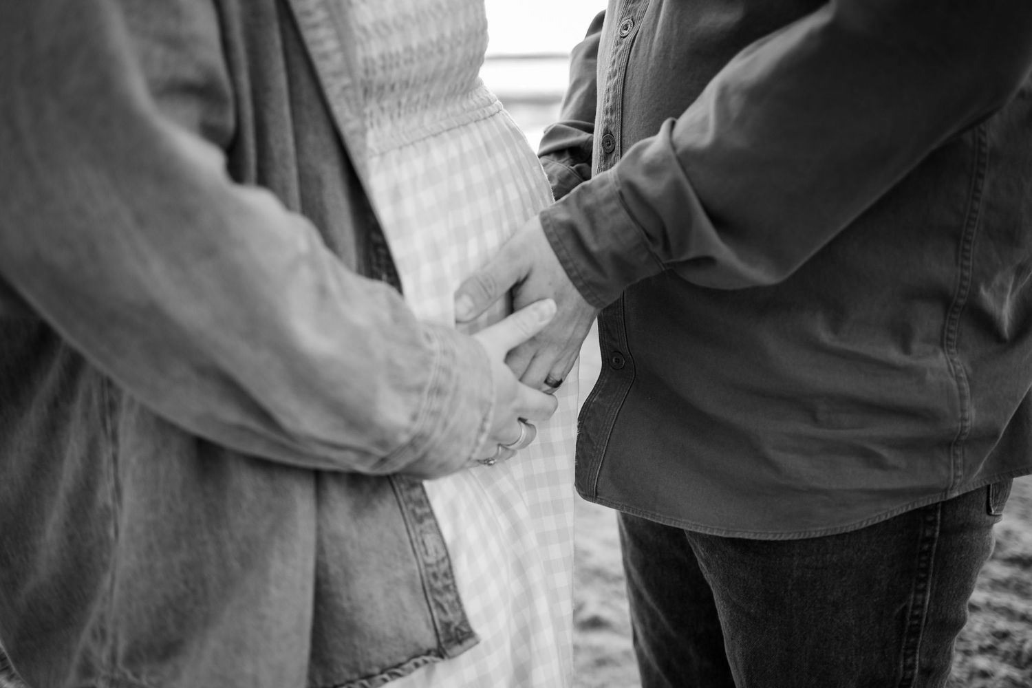 Black and white intimate portrait of couple holding hands on beach.