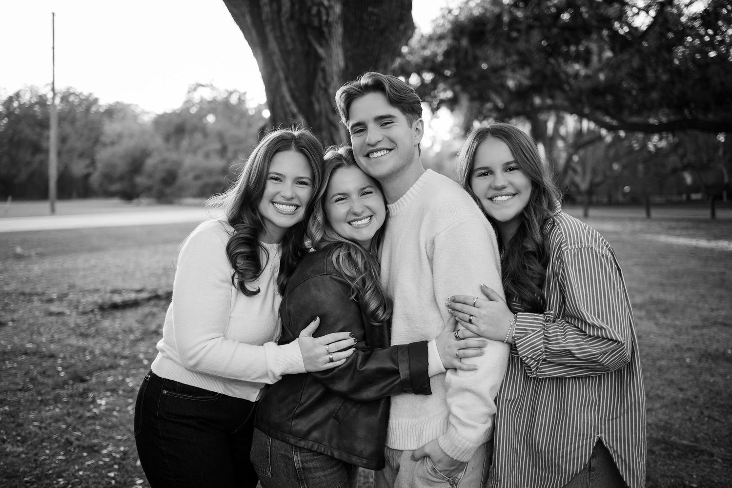 A black and white portrait of a small group hugging and smiling under a tree.