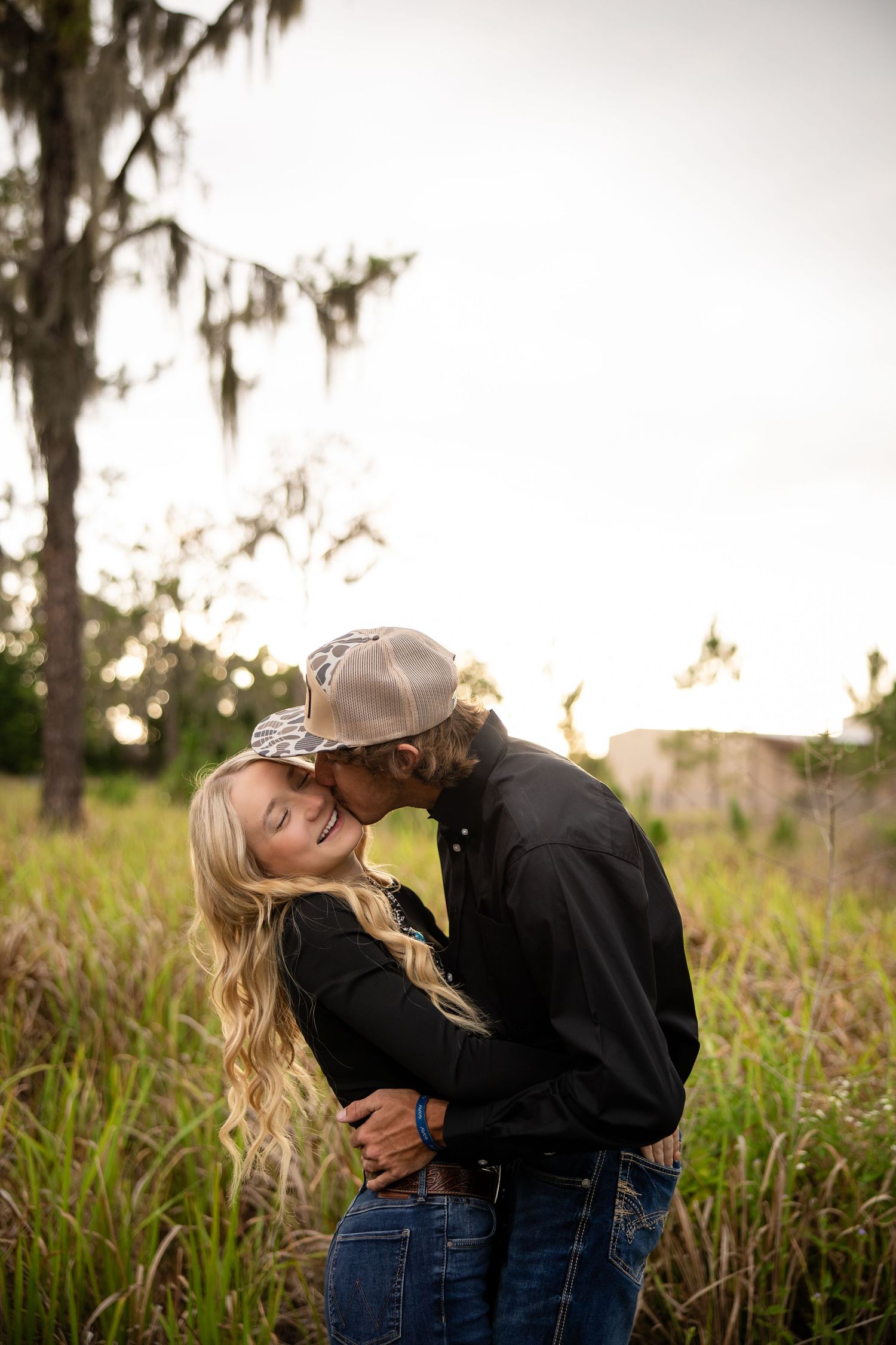 Couple sharing a romantic kiss in a sunlit grassy field, woman with blonde hair leaning back in mans arms.