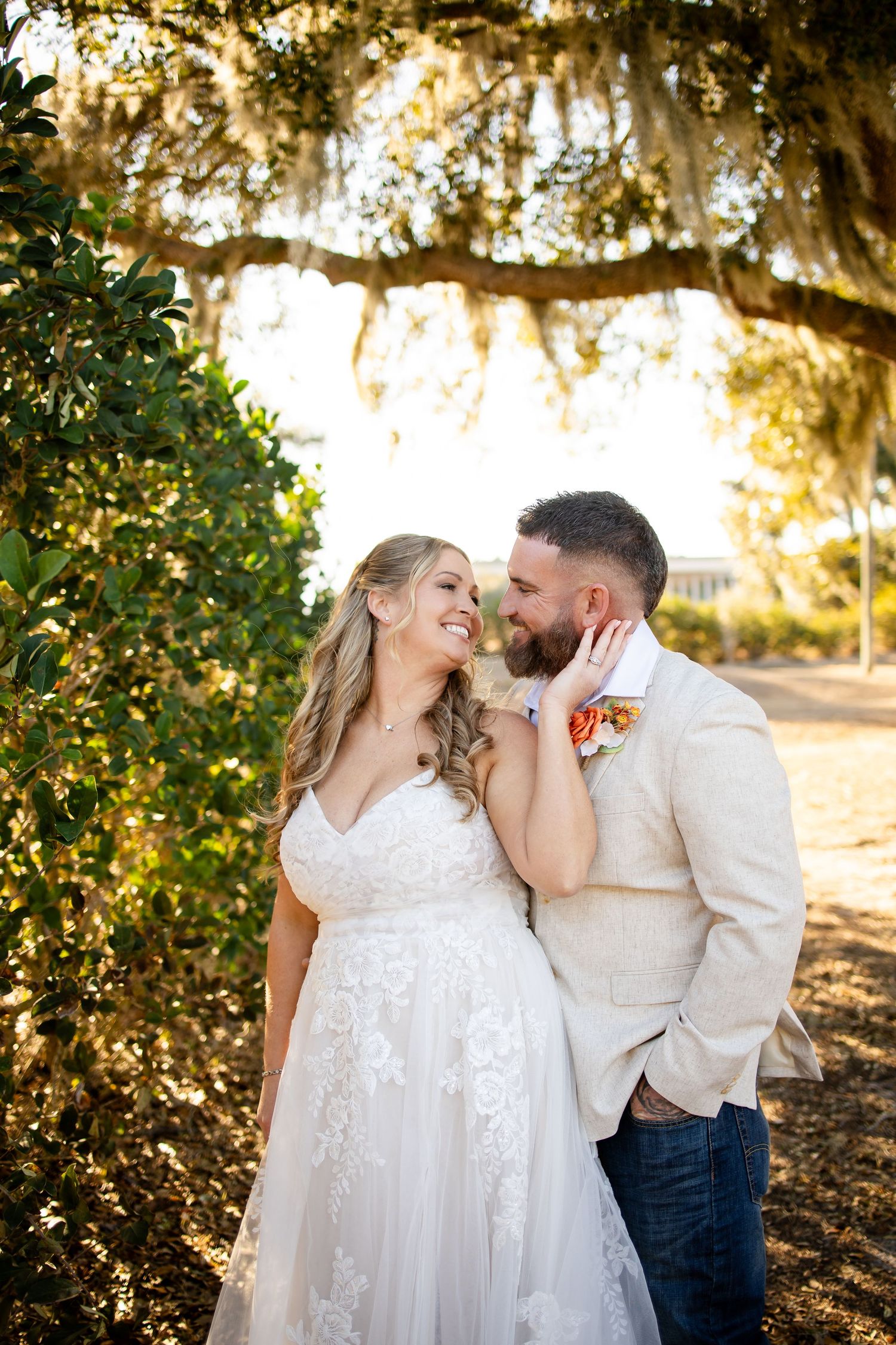 A couple in wedding attire shares intimate moments at sunset under Spanish moss-draped trees.